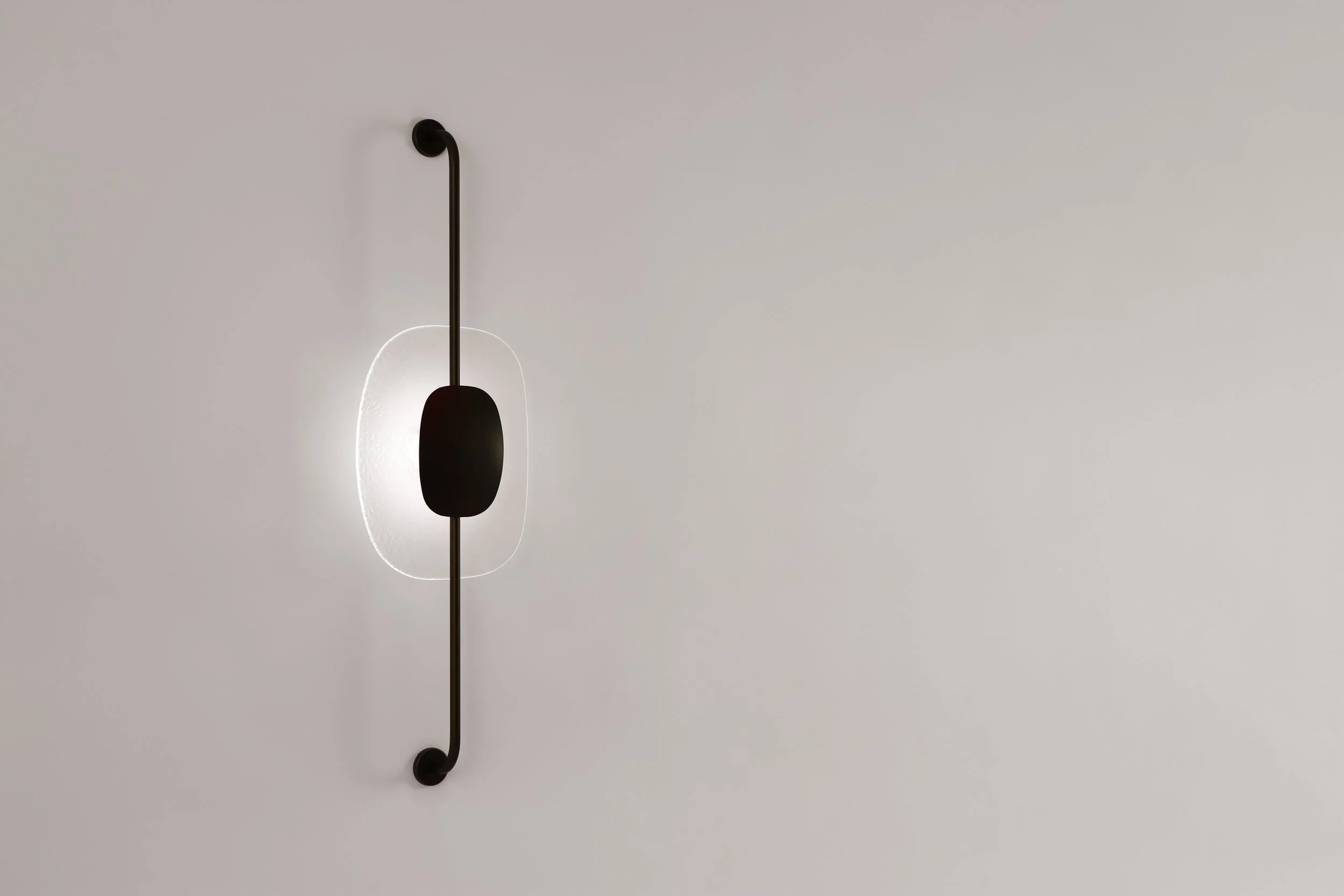 Vertical view of the Drop Light II (Axis) wall sconce by The Touch Studio. Featuring a slender black metallic axis and an amber aquatic-textured glass core. Handcrafted in Italy