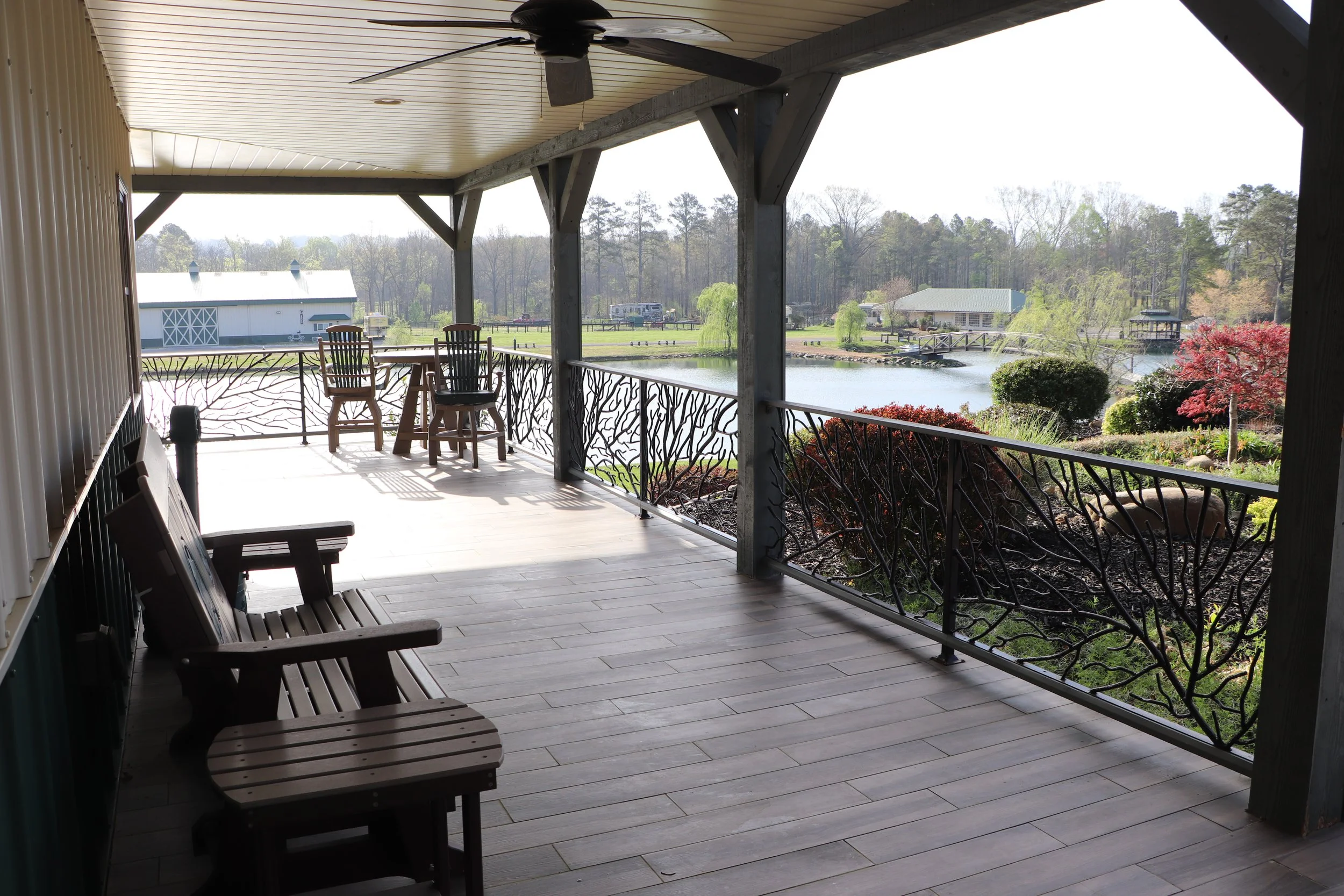 Covered porch overlooking a pond with trees, a building, and a bridge in the background.