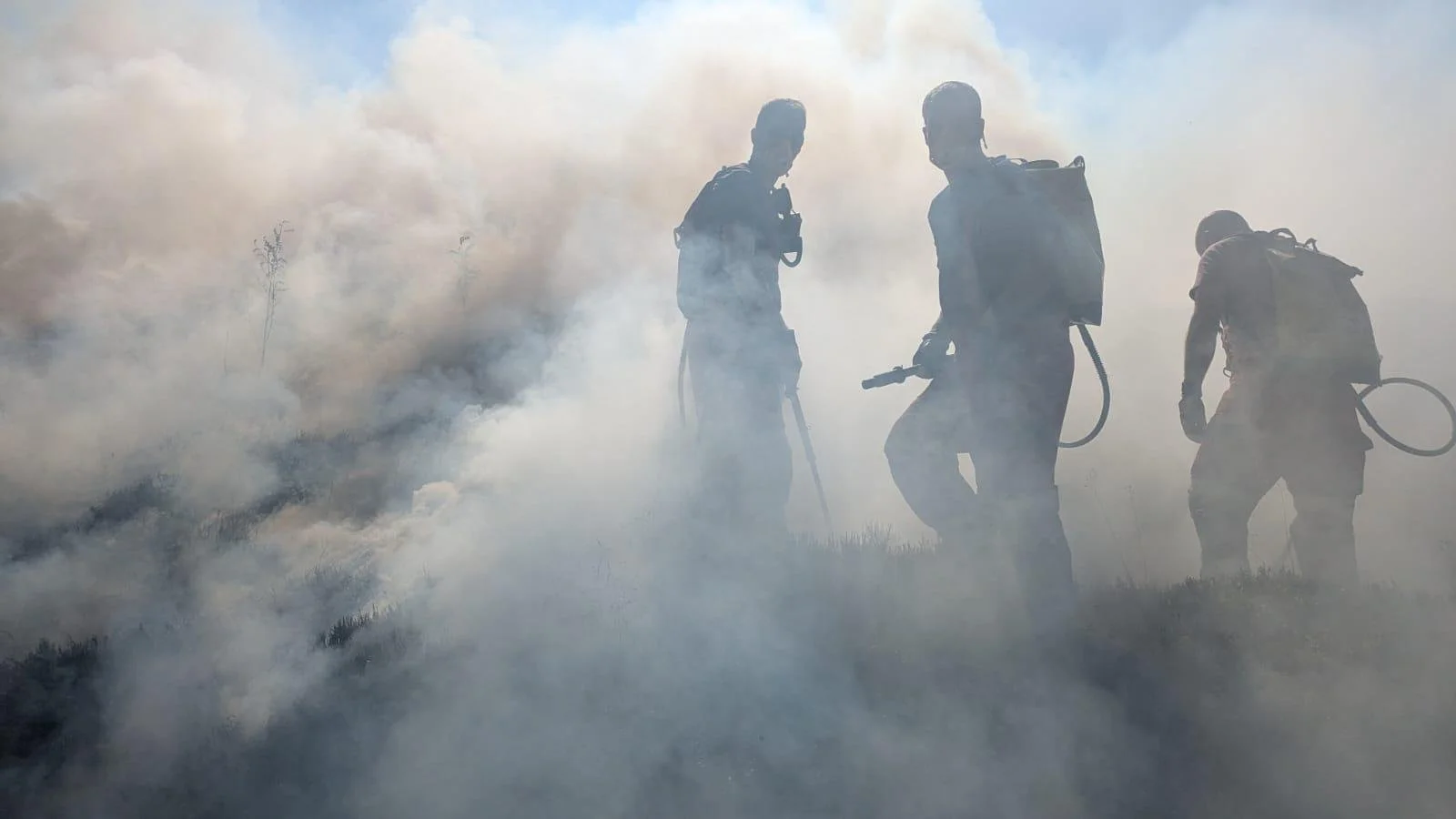 Three figures wreathed in smoke tackling a wildfire