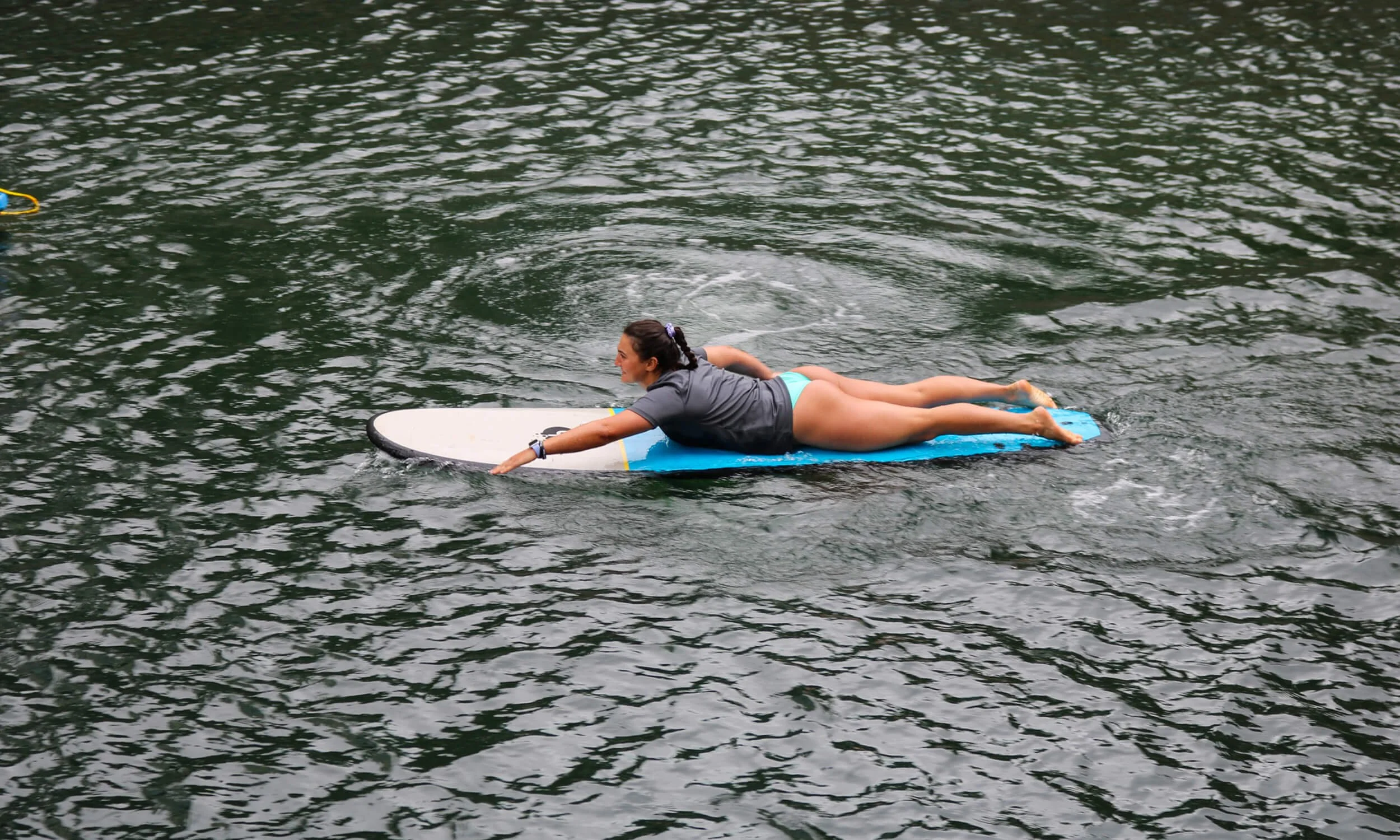 A woman lying flat on a surfboard paddling on the water