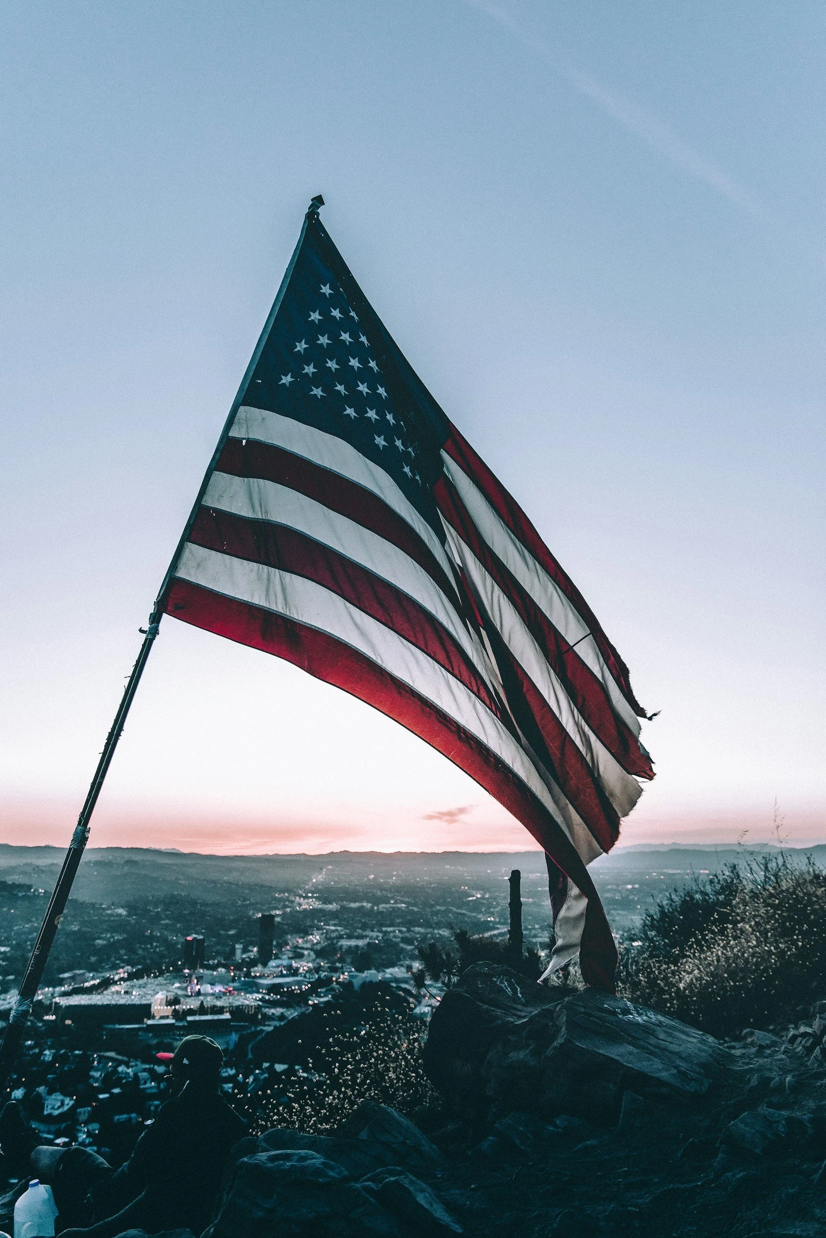 American flag on a hill with cityscape at sunset in background