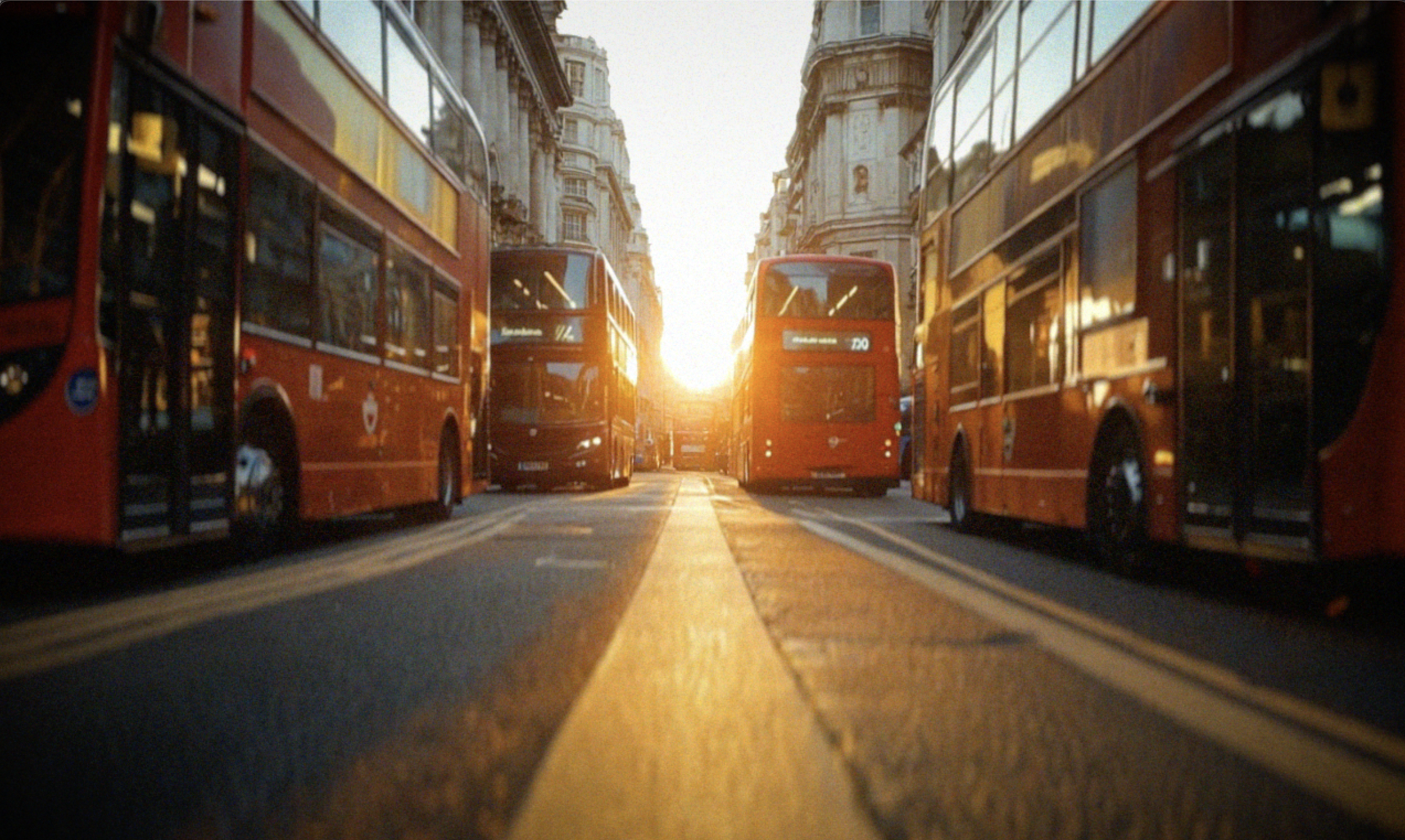Street view of red double-decker buses at sunset in a city with historic buildings on the sides.