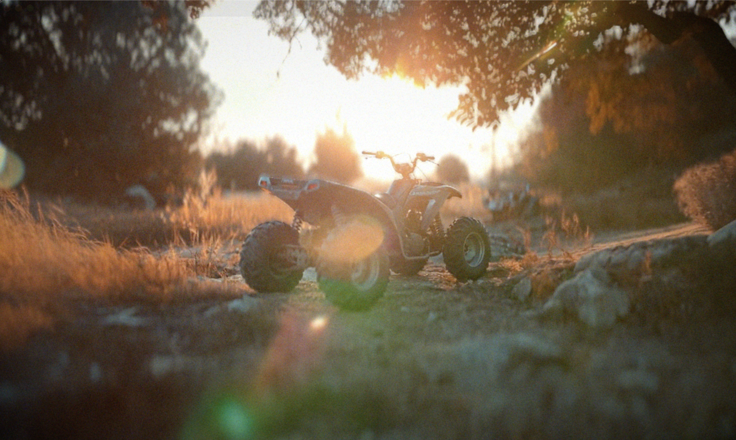 A quad bike parked on a dirt trail with the sun setting behind trees, creating a lens flare.
