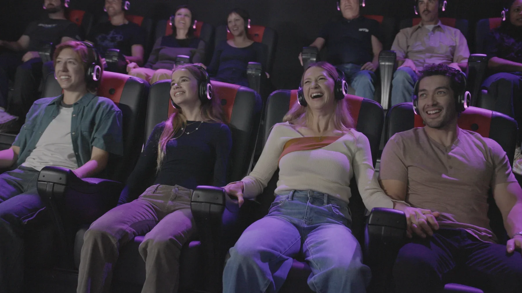 People in a movie theater wearing 3D glasses, sitting in stadium seats, smiling and enjoying the film.