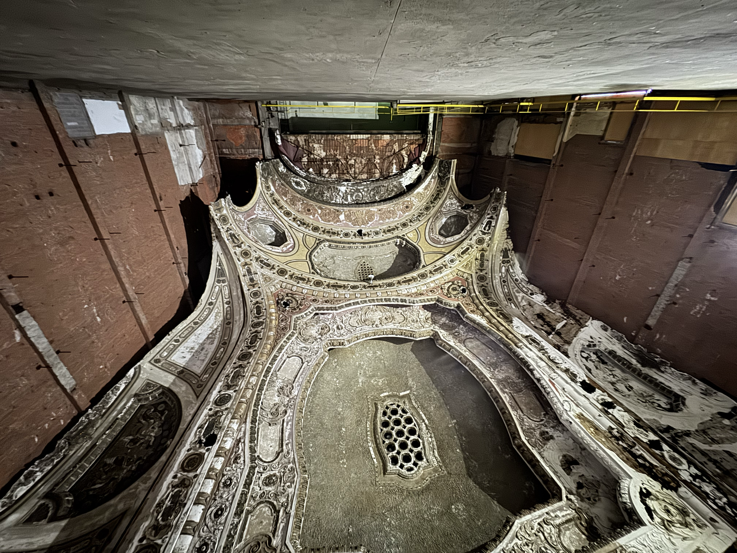 An ornate, decorated ceiling and partial wall restoration in progress, with exposed bricks and a section of decorative plasterwork, in an interior space under renovation.