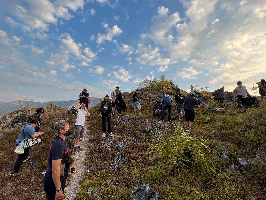 Group of hikers on a hilltop trail with a cloudy sky in the background, some wearing masks and carrying backpacks.