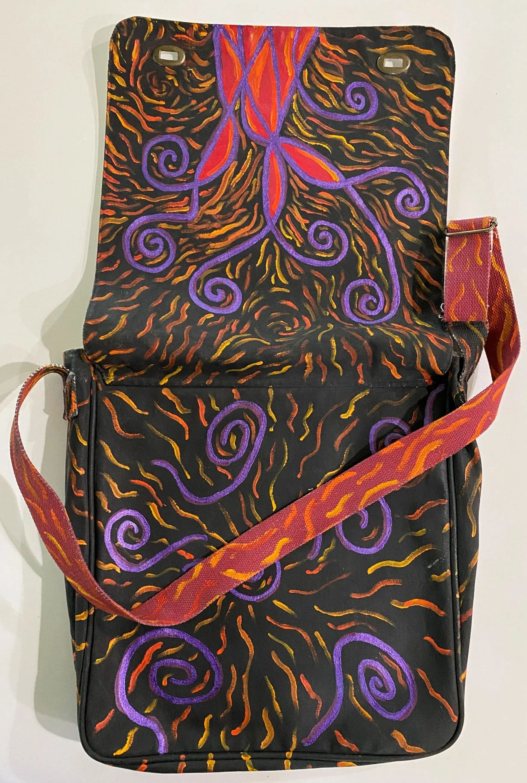 Black backpack with colorful swirling and leaf patterns in purple, orange, red, and yellow, featuring a red and purple strap.