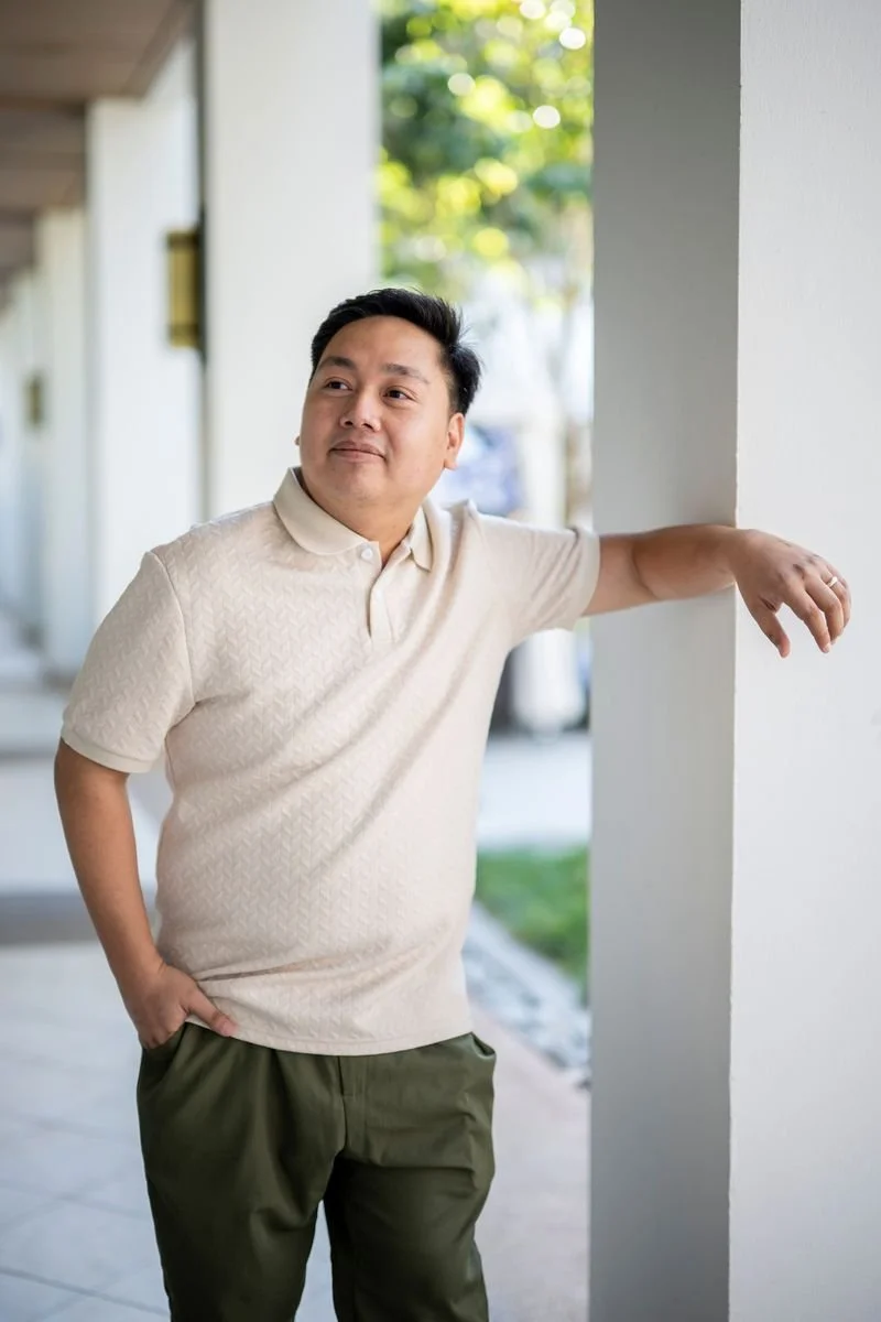 Portrait of a man in a black suit and tie against a solid light blue background.