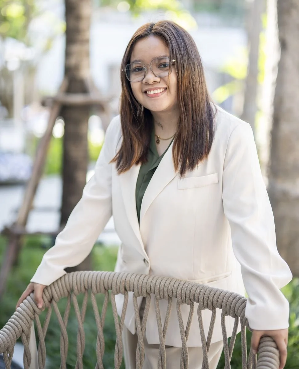 Professional woman smiling in formal business attire against a mint green background.