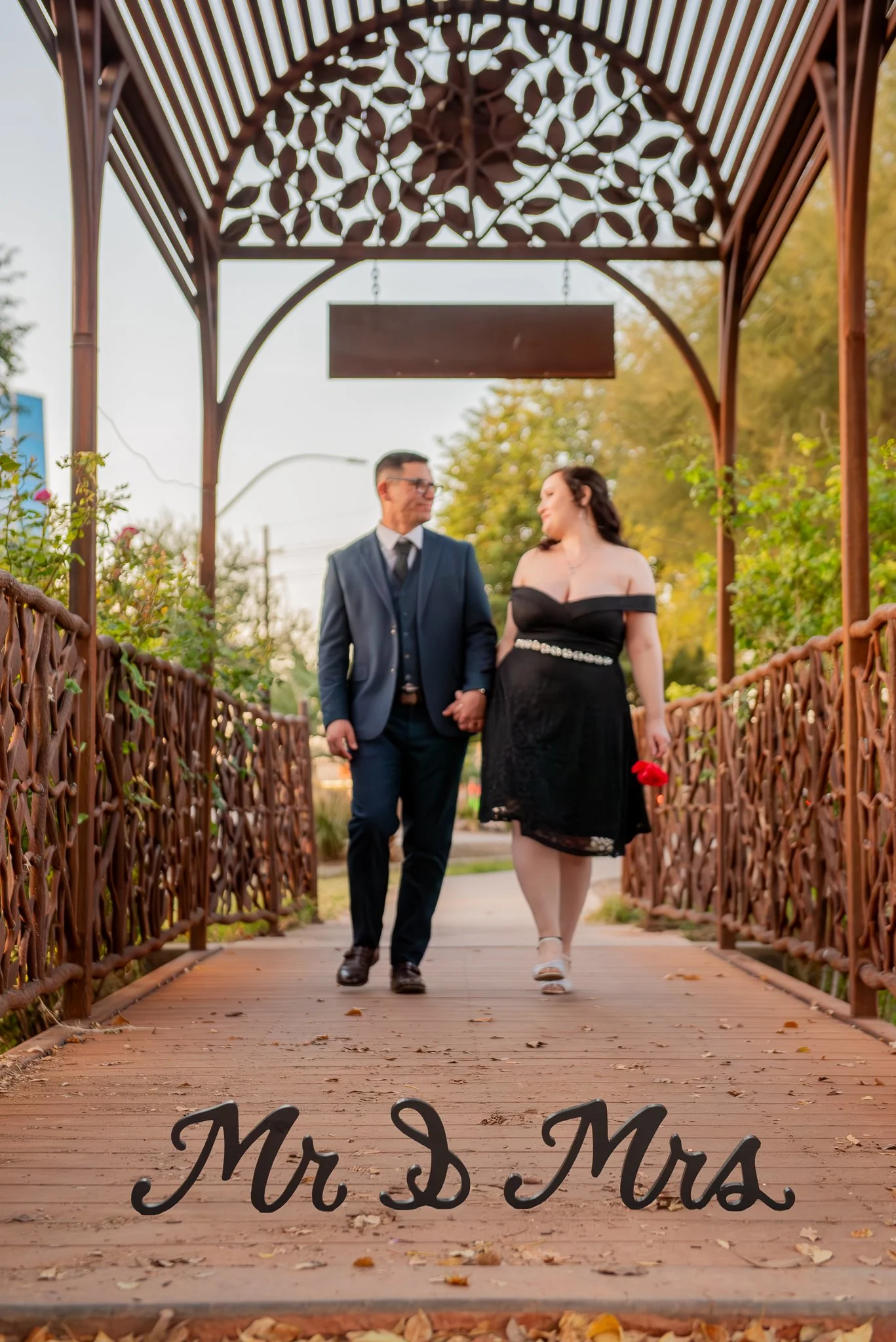 Couple walk hand-in-hand on a bridge at the MCC Rose Garden at Sunset