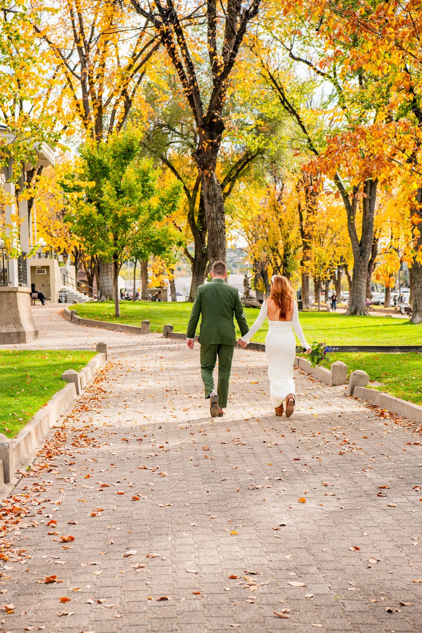  Action image featuring the eloping bride and groom walking hand-in-hand at the Yavapai Courthouse in Downtown Prescott, Arizona during their destination adventure elopement. 