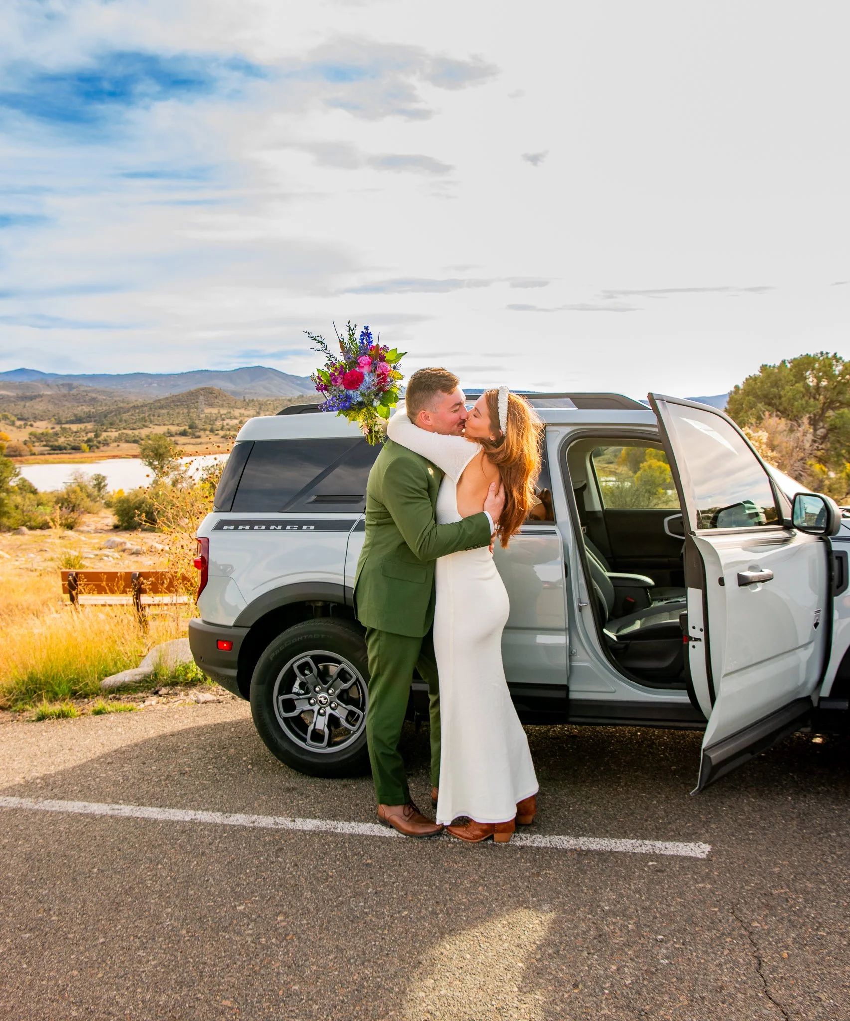 Bride and groom kiss and hold each other in front of their Ford Bronco at Watson Lake in Prescott, Arizona during their destination adventure elopement.
