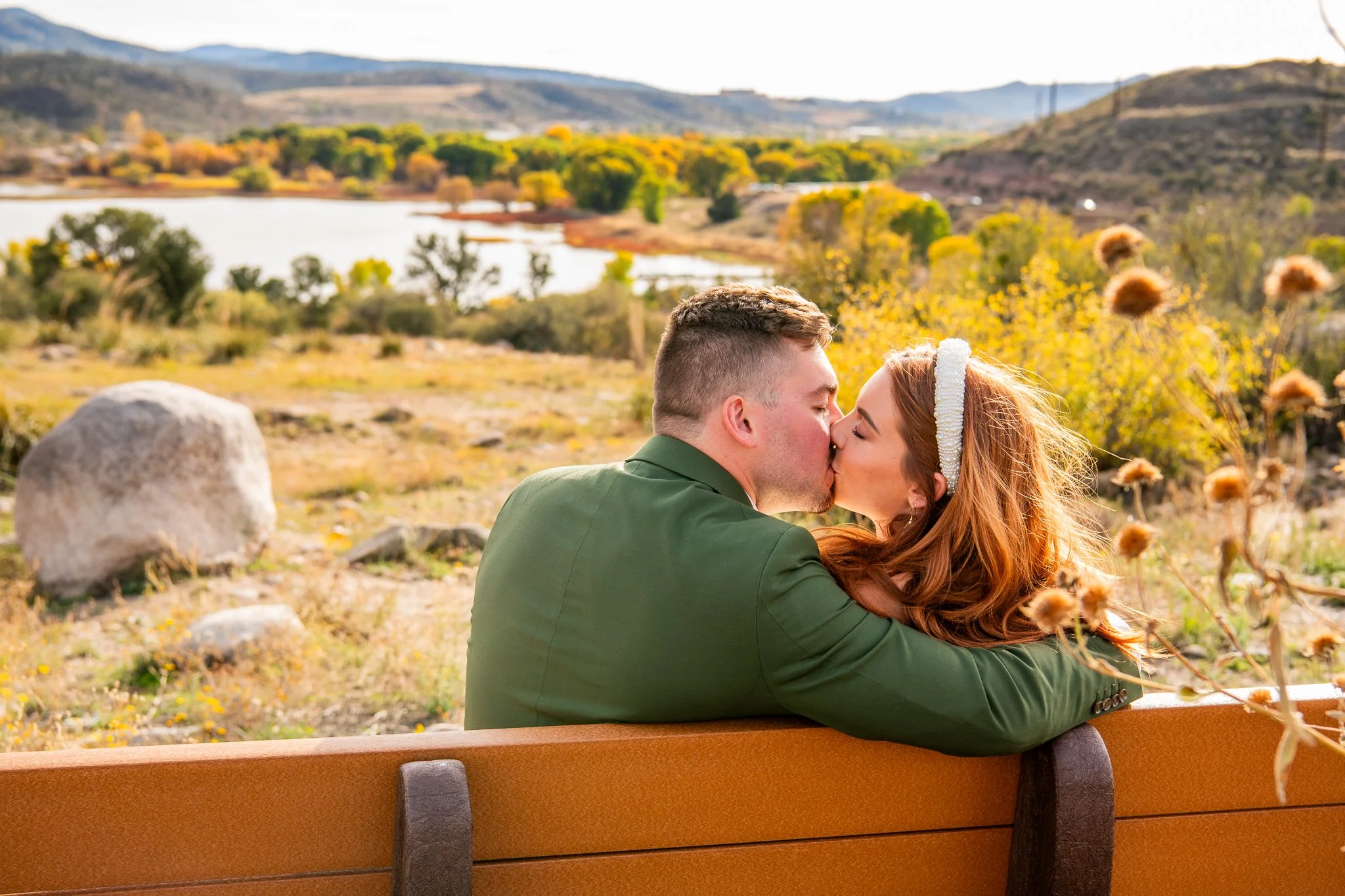 Close up image of bride and groom kissing on a bench with Watson Lake and the unique desert landscape around them in Prescott, Arizona during their destination adventure elopement.