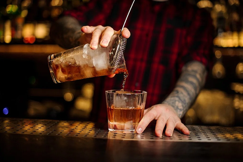 Bartender pouring a cocktail with ice into a glass at a bar