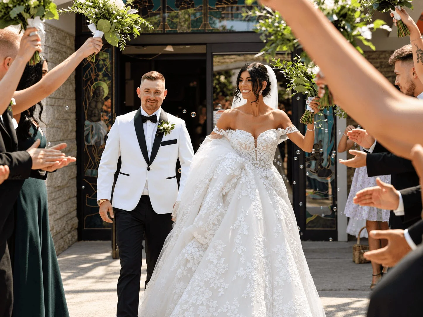 Bride and groom walking past cheering wedding guests as bouquets are raised around them.