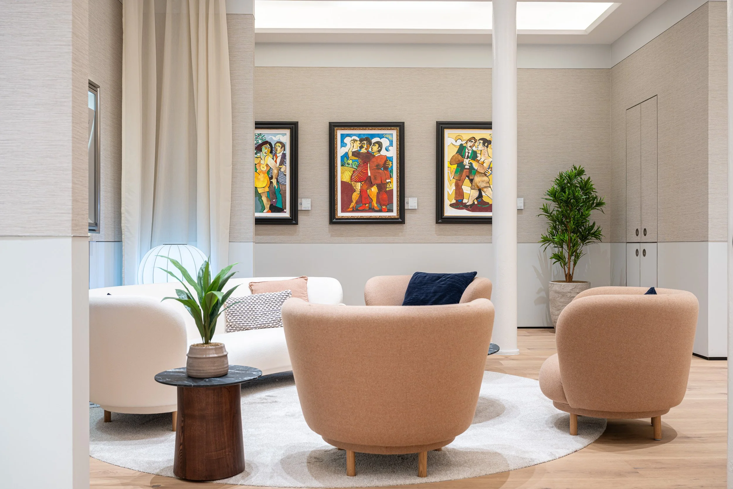 Three framed paintings behind pale pink lounge chairs and white columns.