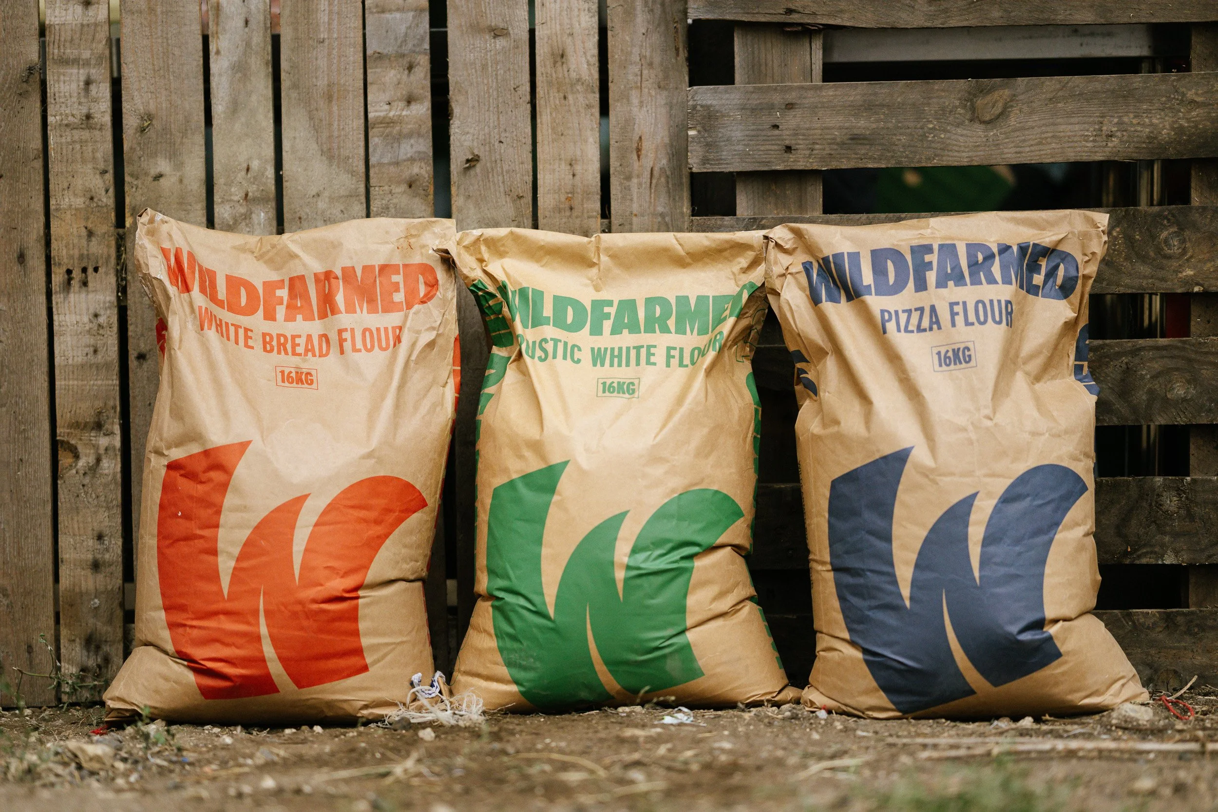 Three sacks of Wildfarmed flour in front of stacked wooden pallets.