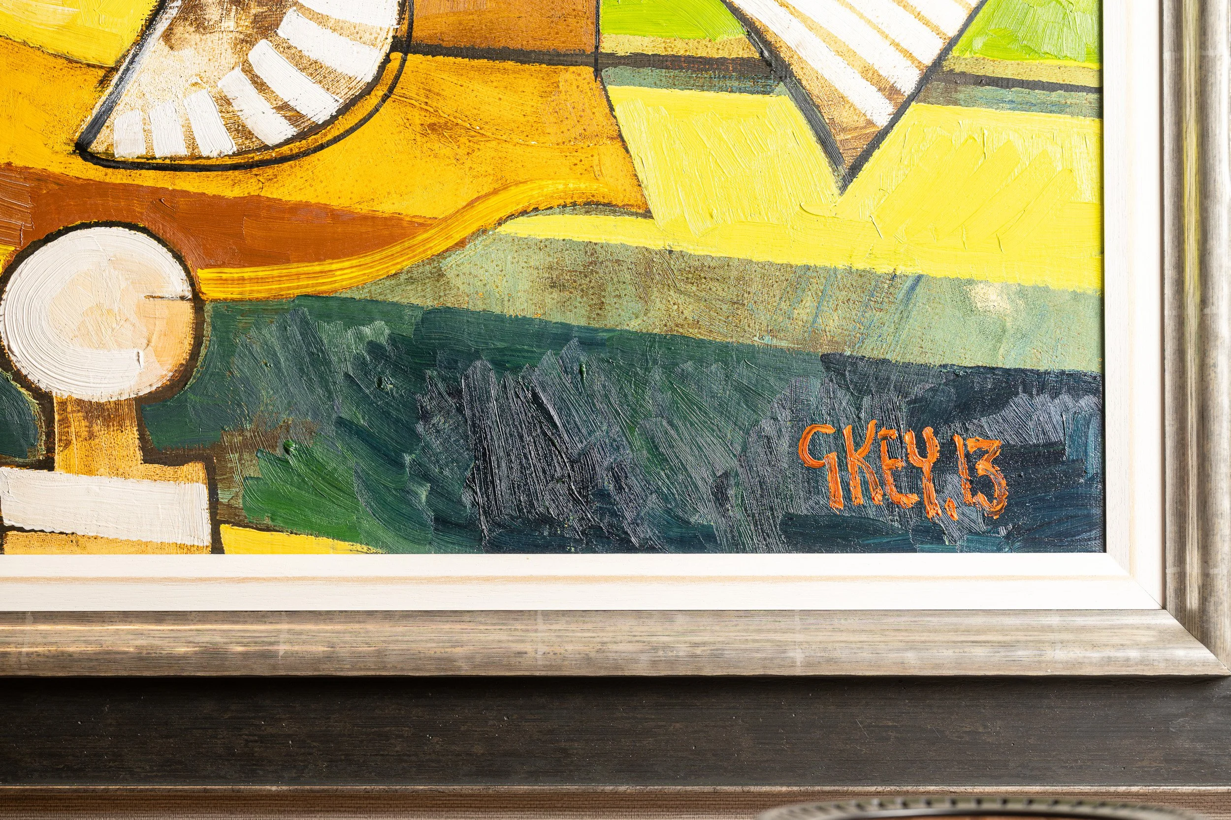 Close-up of yellow and green paint, an orange signature and the edge of a picture frame.