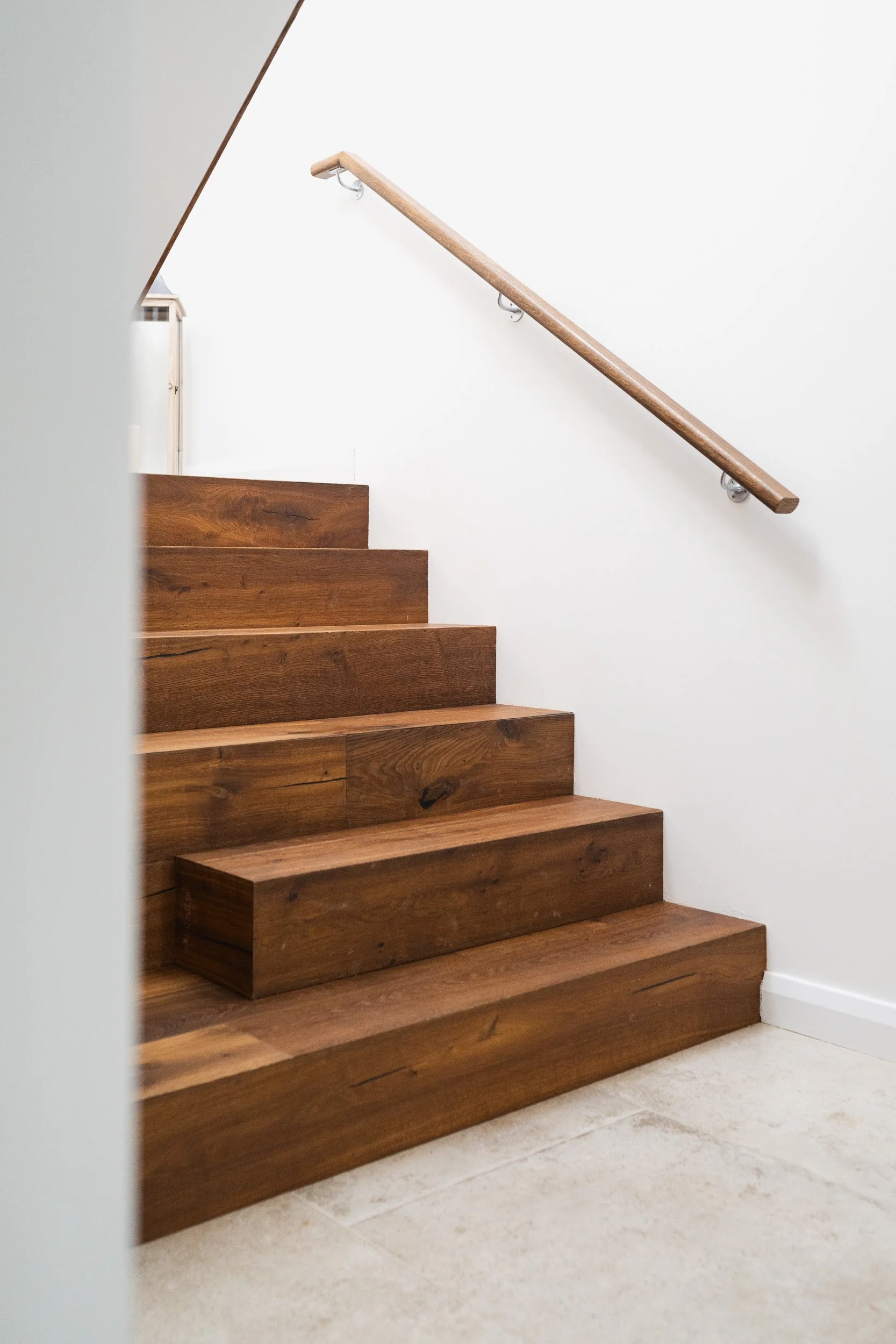 Timber steps rising beside a white wall with a wooden handrail.