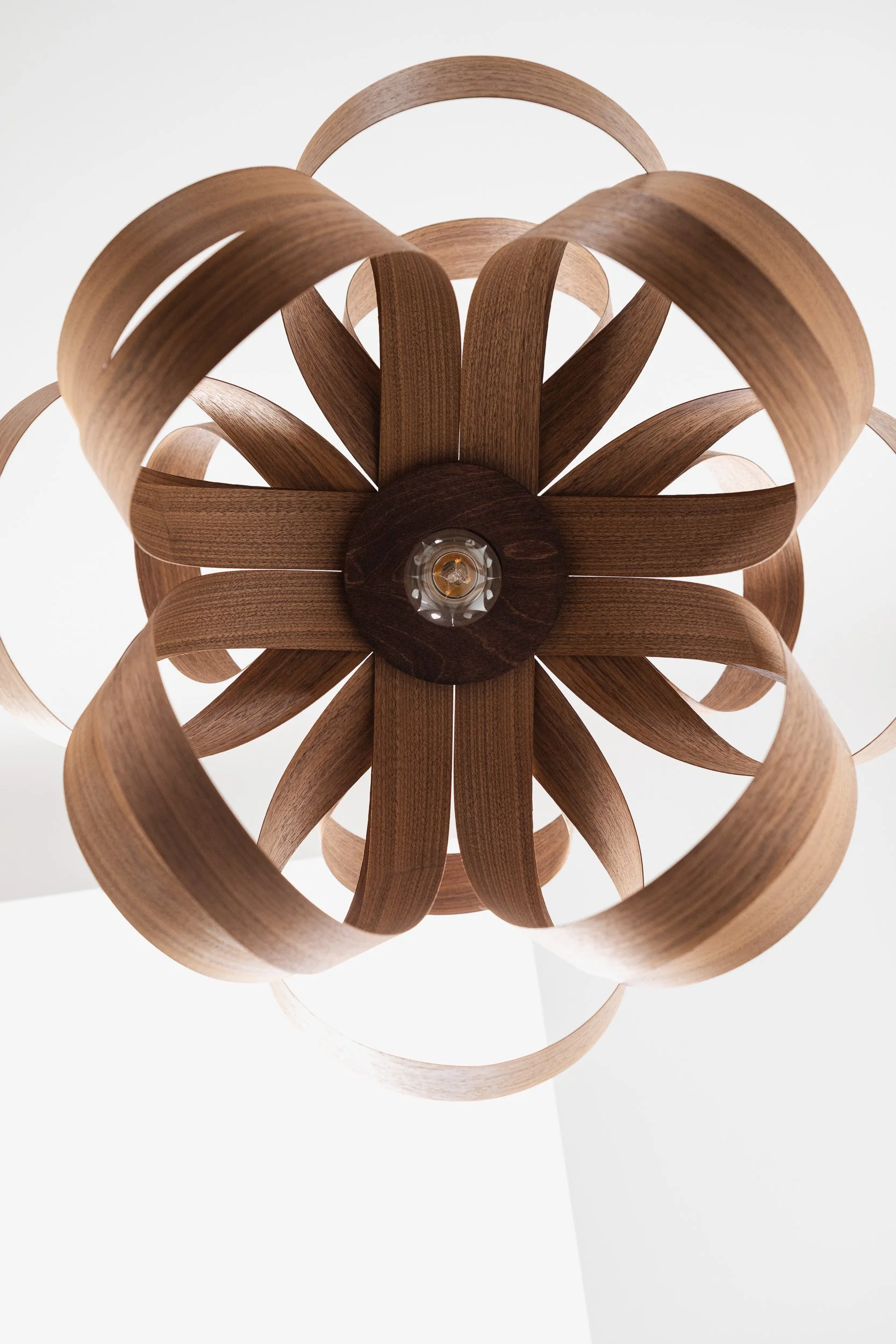 Upward view of a pendant light formed from curved wooden loops around a central bulb.