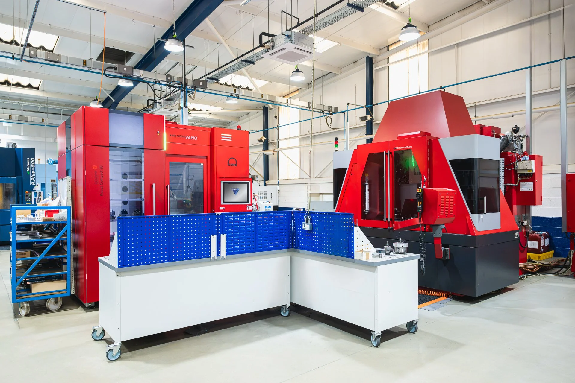 Red industrial machines and blue storage equipment beneath the factory’s high ceiling.
