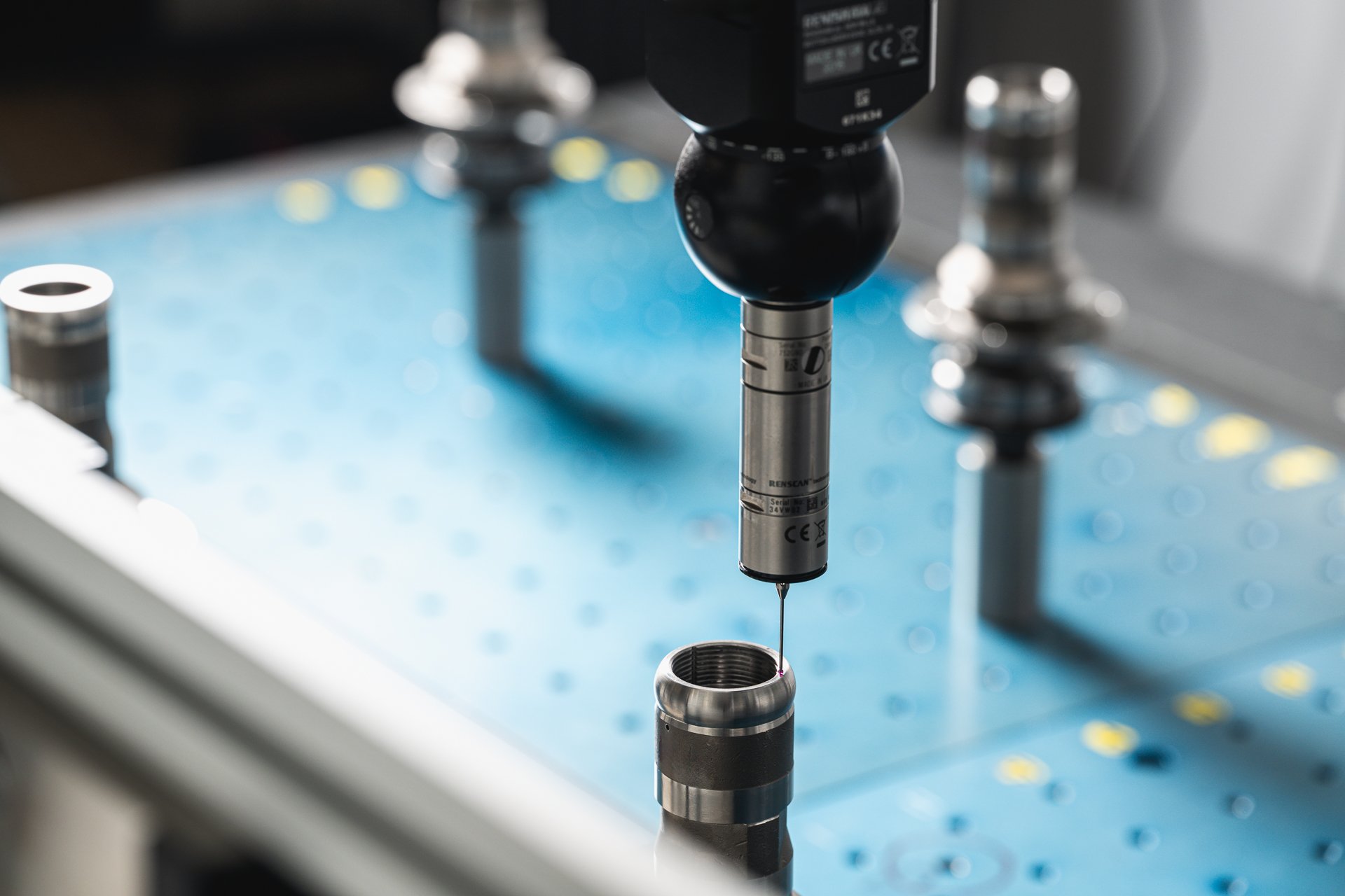 Inspection probe positioned above a cylindrical metal component on a blue measuring table.