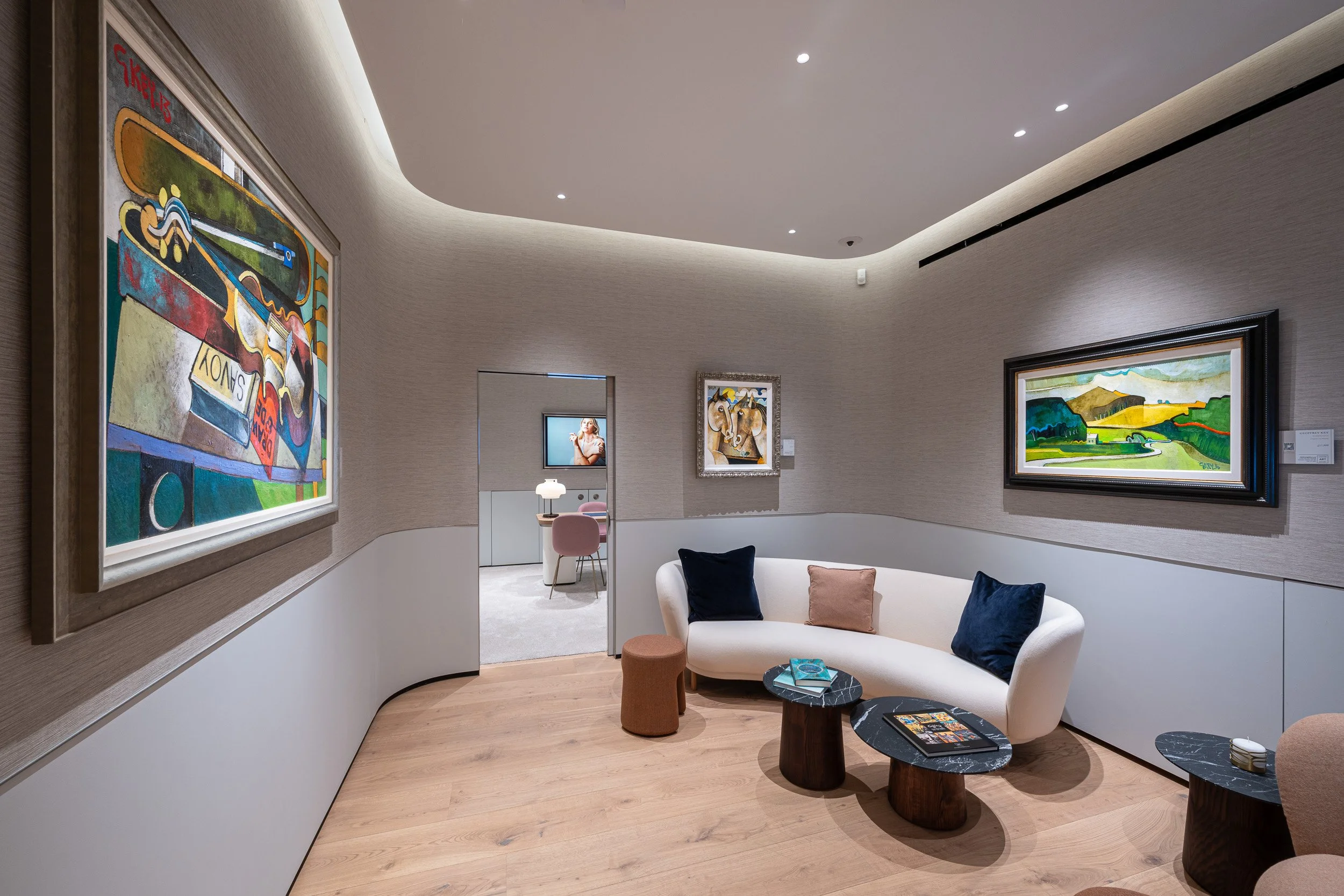 Framed paintings around a lounge with a pale sofa, blue cushions and small tables.