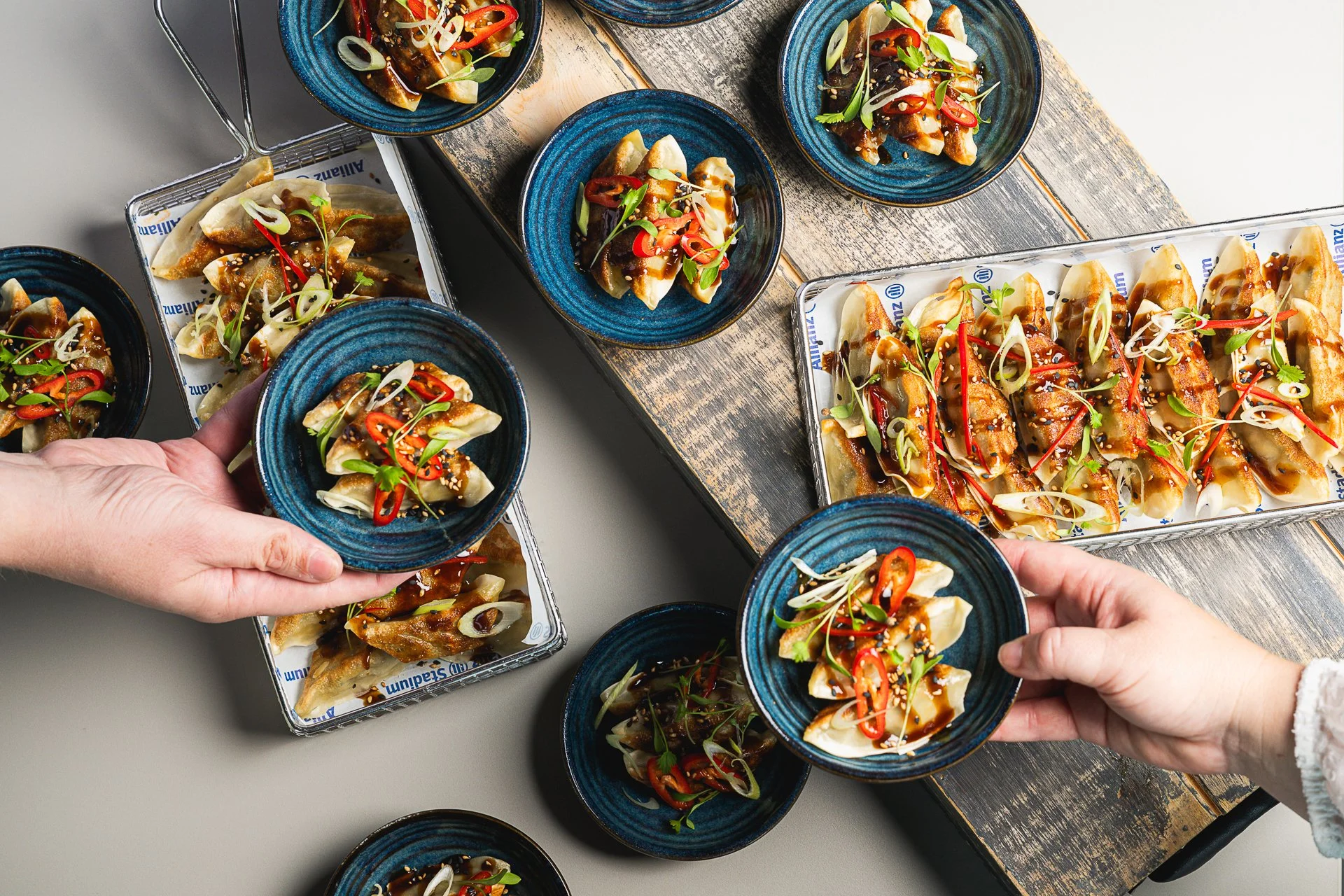 Overhead view of hands holding blue bowls above a table of food and serving baskets.