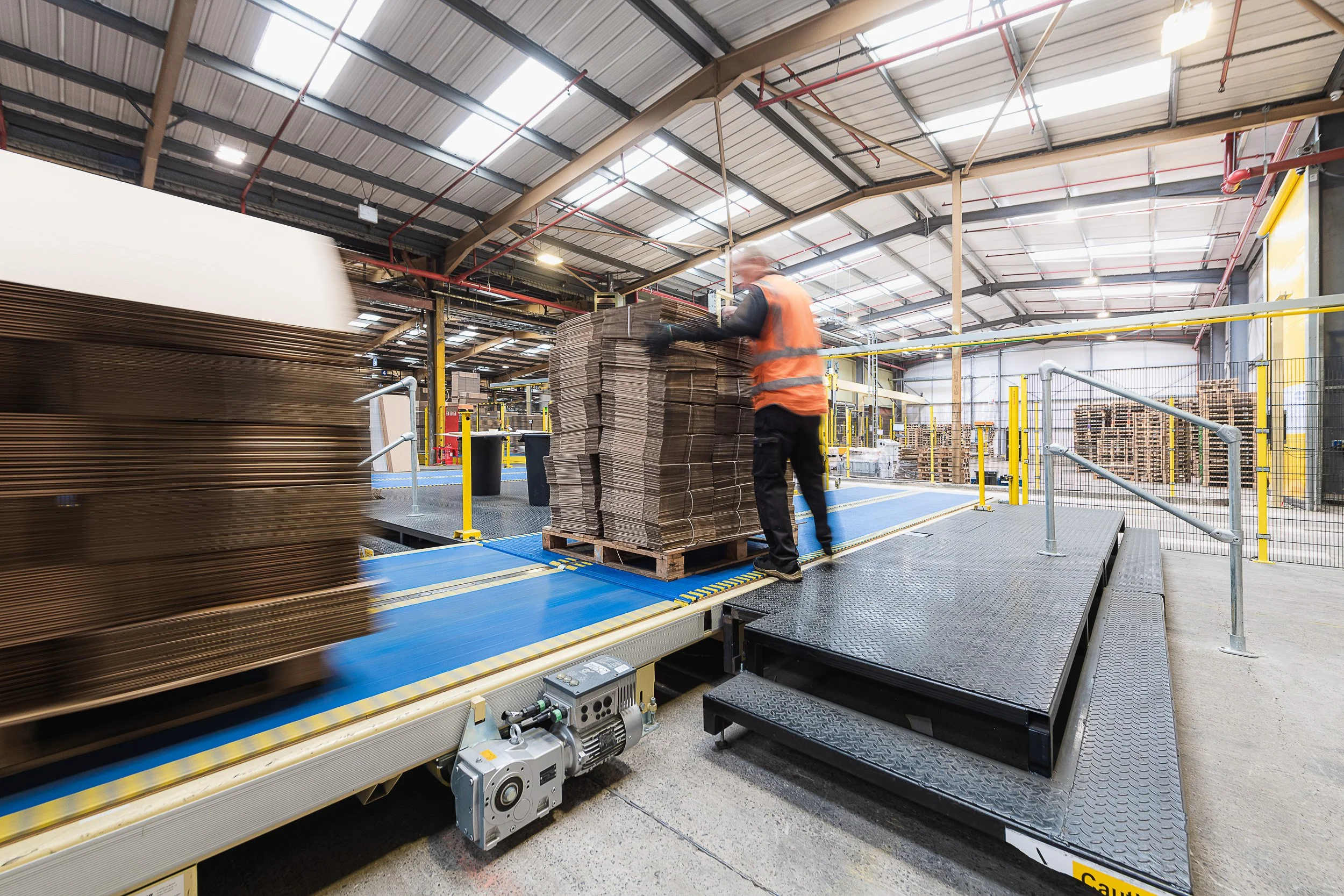 Worker handling stacks of cardboard on a production line inside a factory.