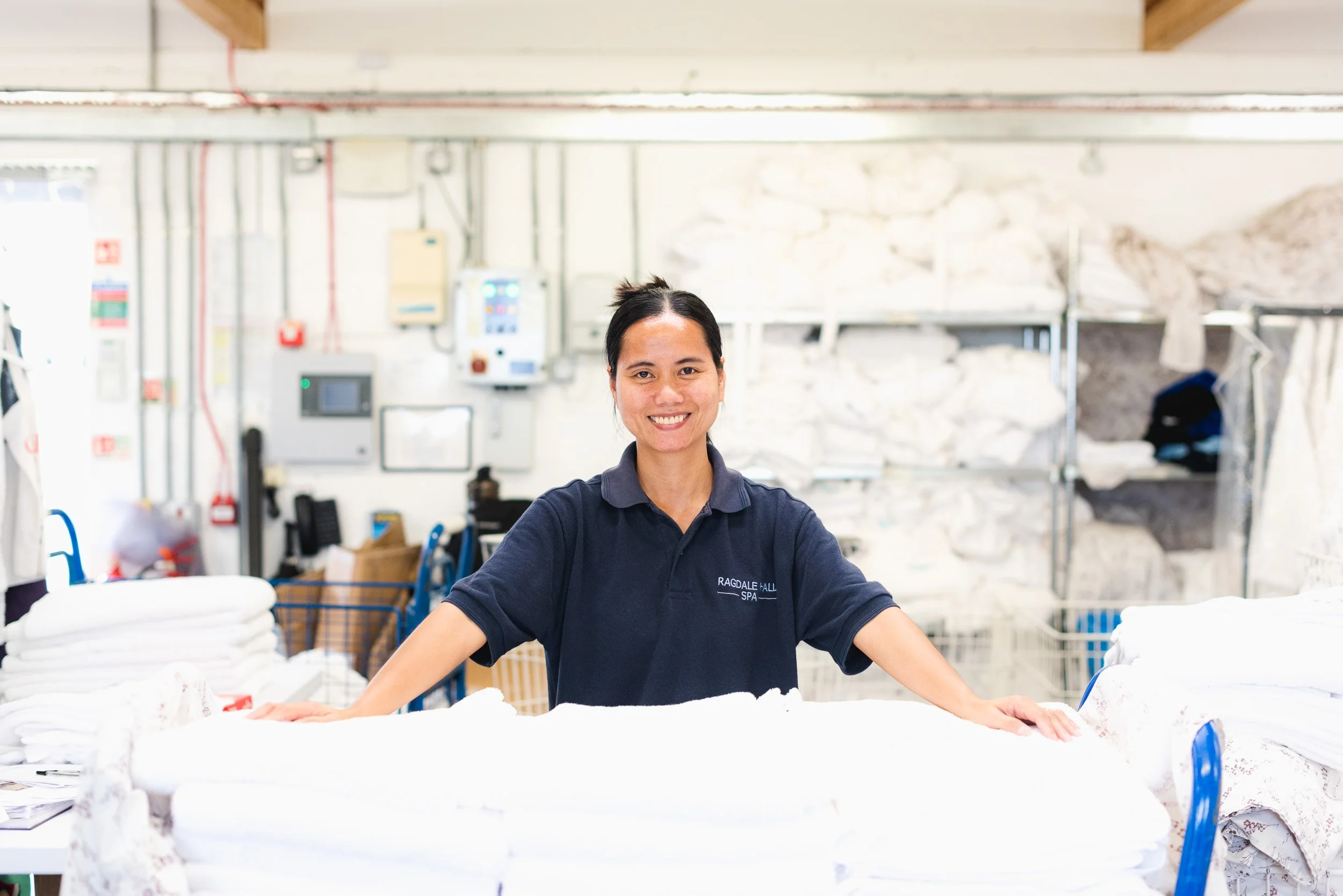 Worker standing behind stacks of linen in a commercial laundry.