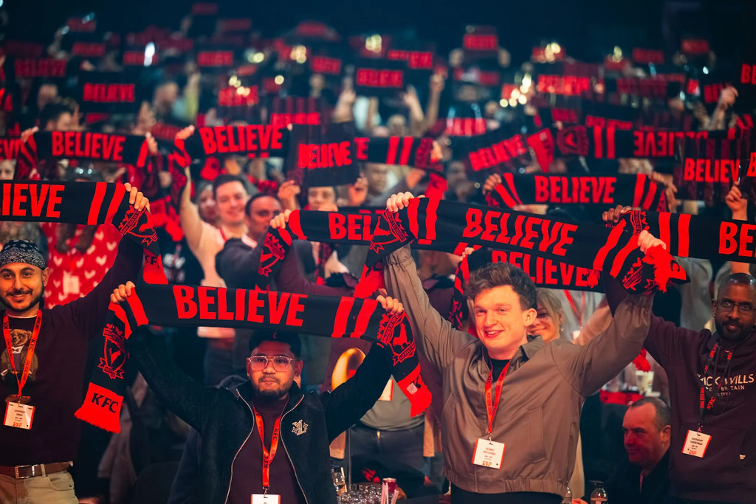 KFC conference delegates holding red and black BELIEVE scarves above their heads.
