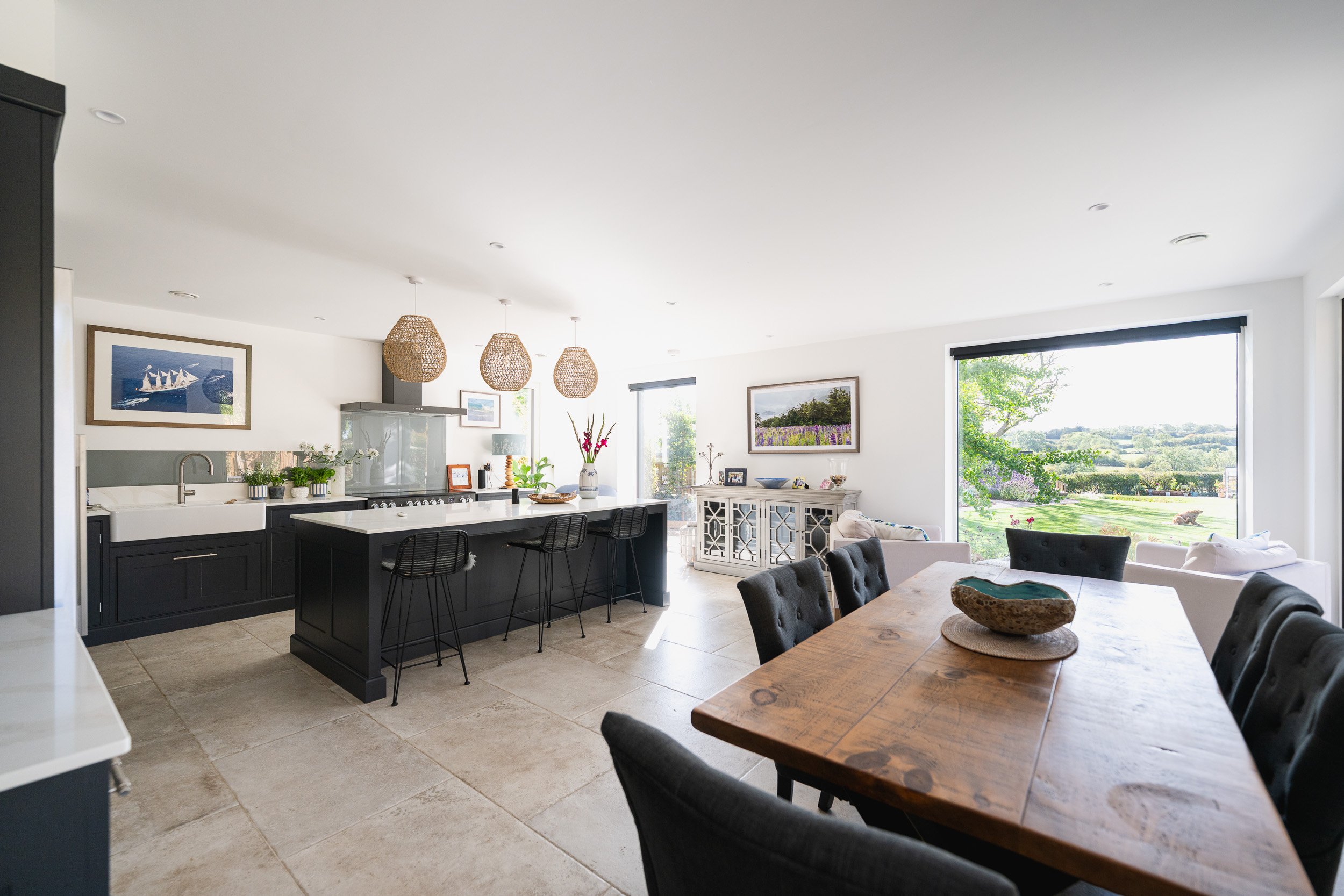 Open-plan kitchen and dining room with dark cabinets, an island, a wooden table and a large garden-facing window.