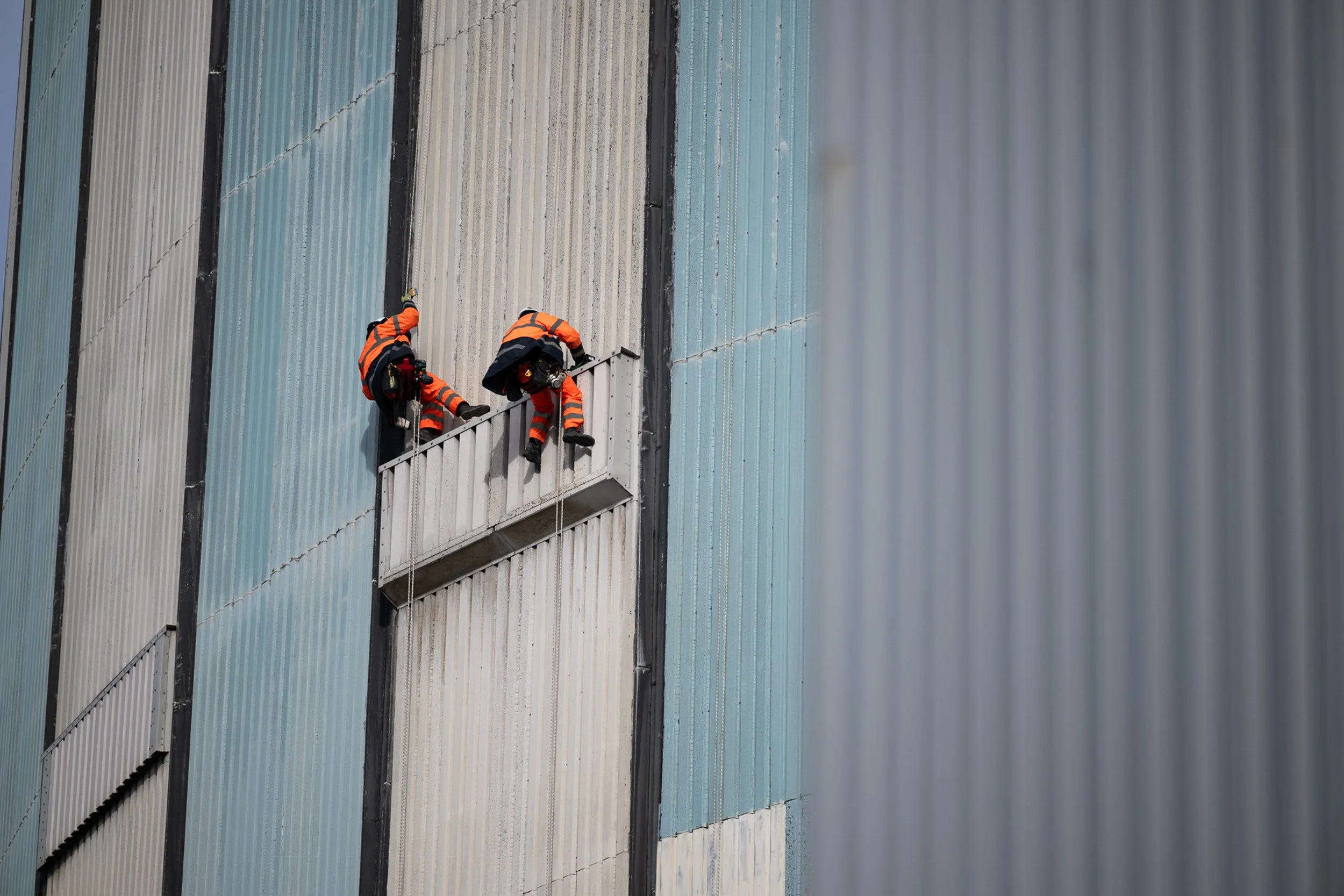 Two rope-access workers on the exterior of an industrial building.