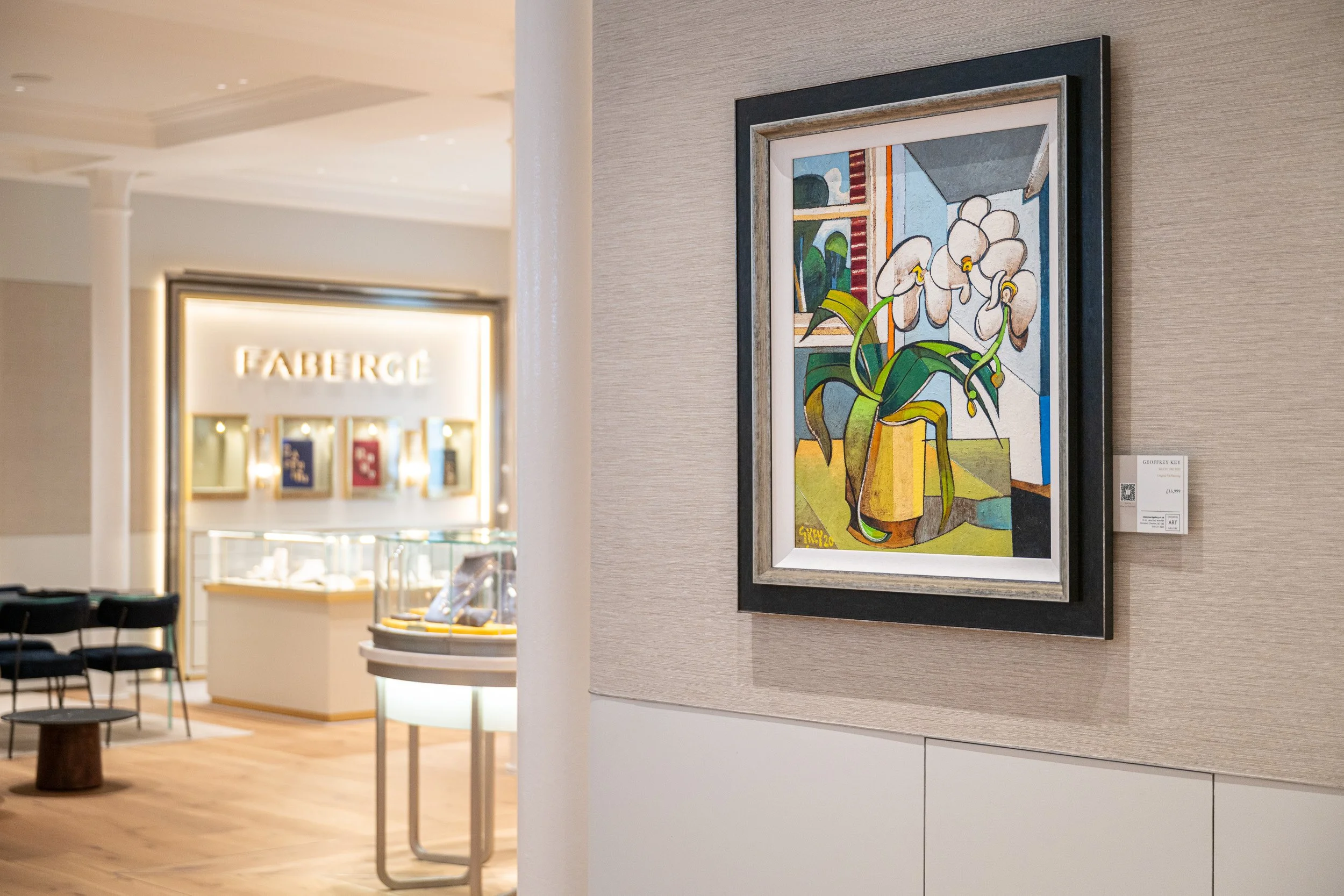 Framed floral painting with an illuminated Fabergé display visible beyond.
