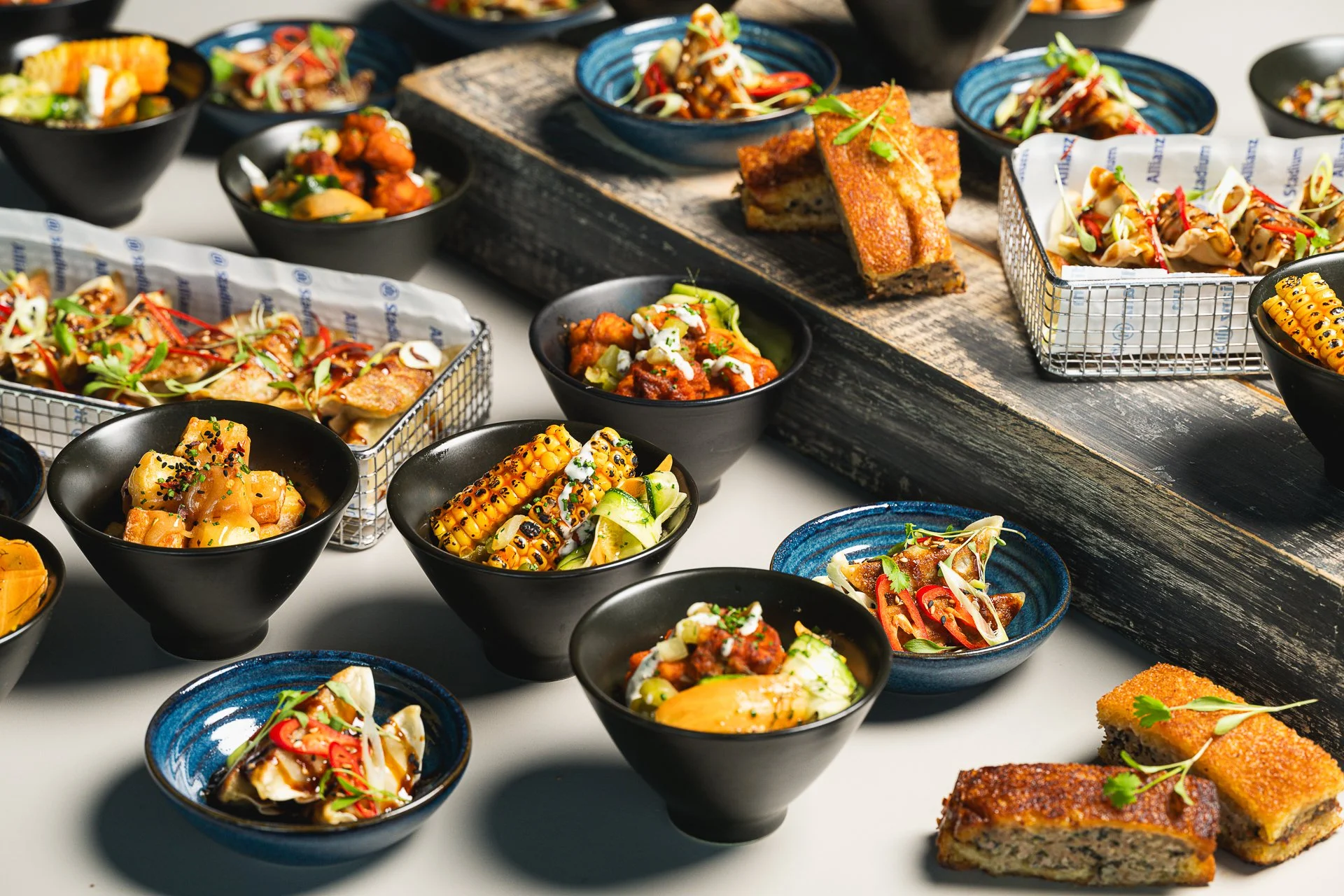 Bowls of food, pastries and serving baskets arranged across a table and raised wooden boards.