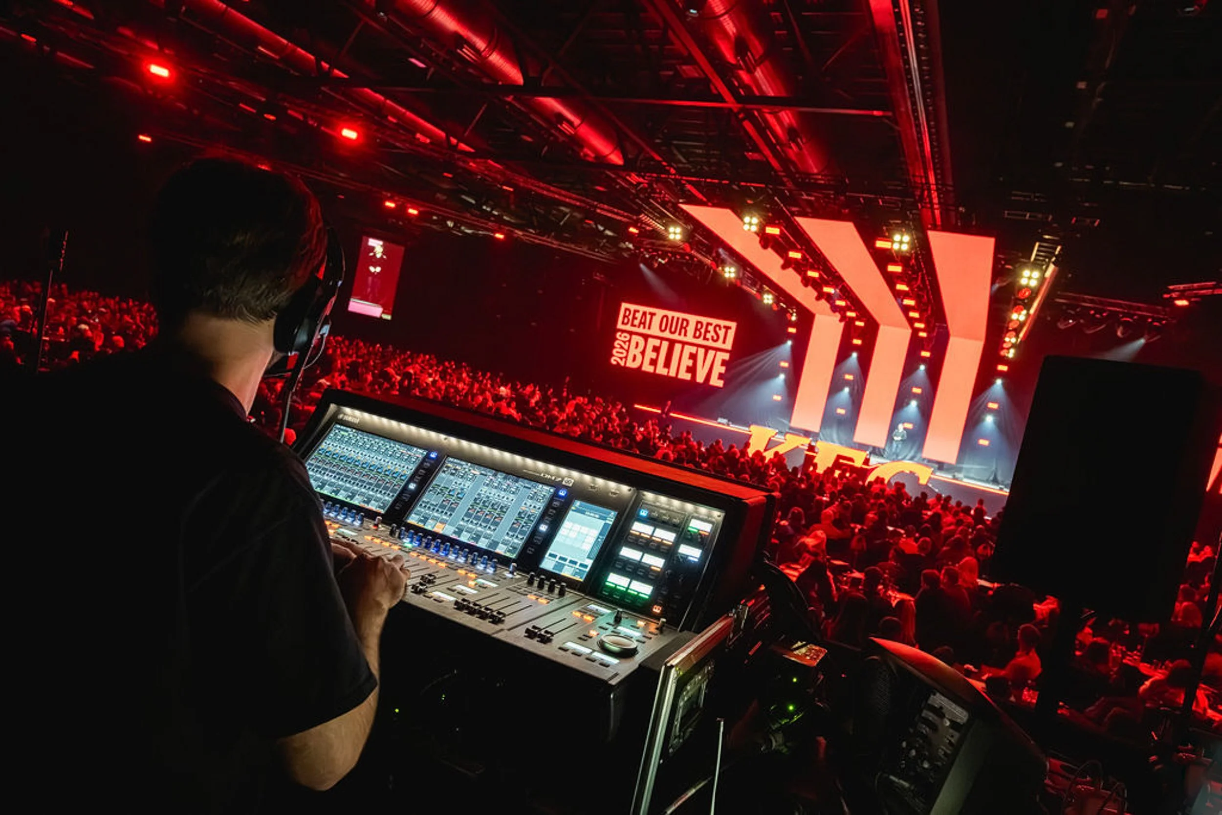 An operator at a control console overlooking the KFC conference stage and audience.