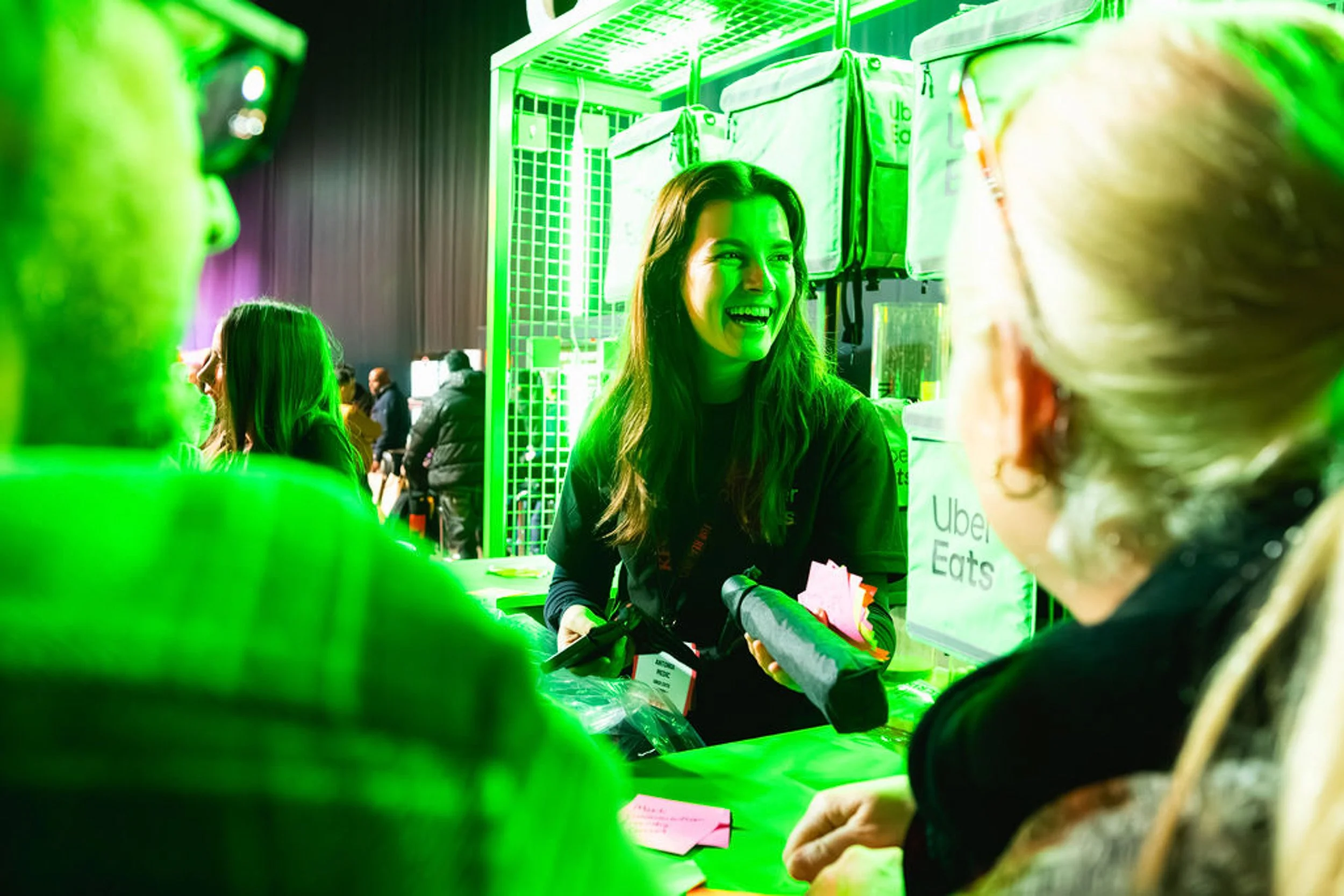 People chatting at the Uber Eats stand under green lighting.