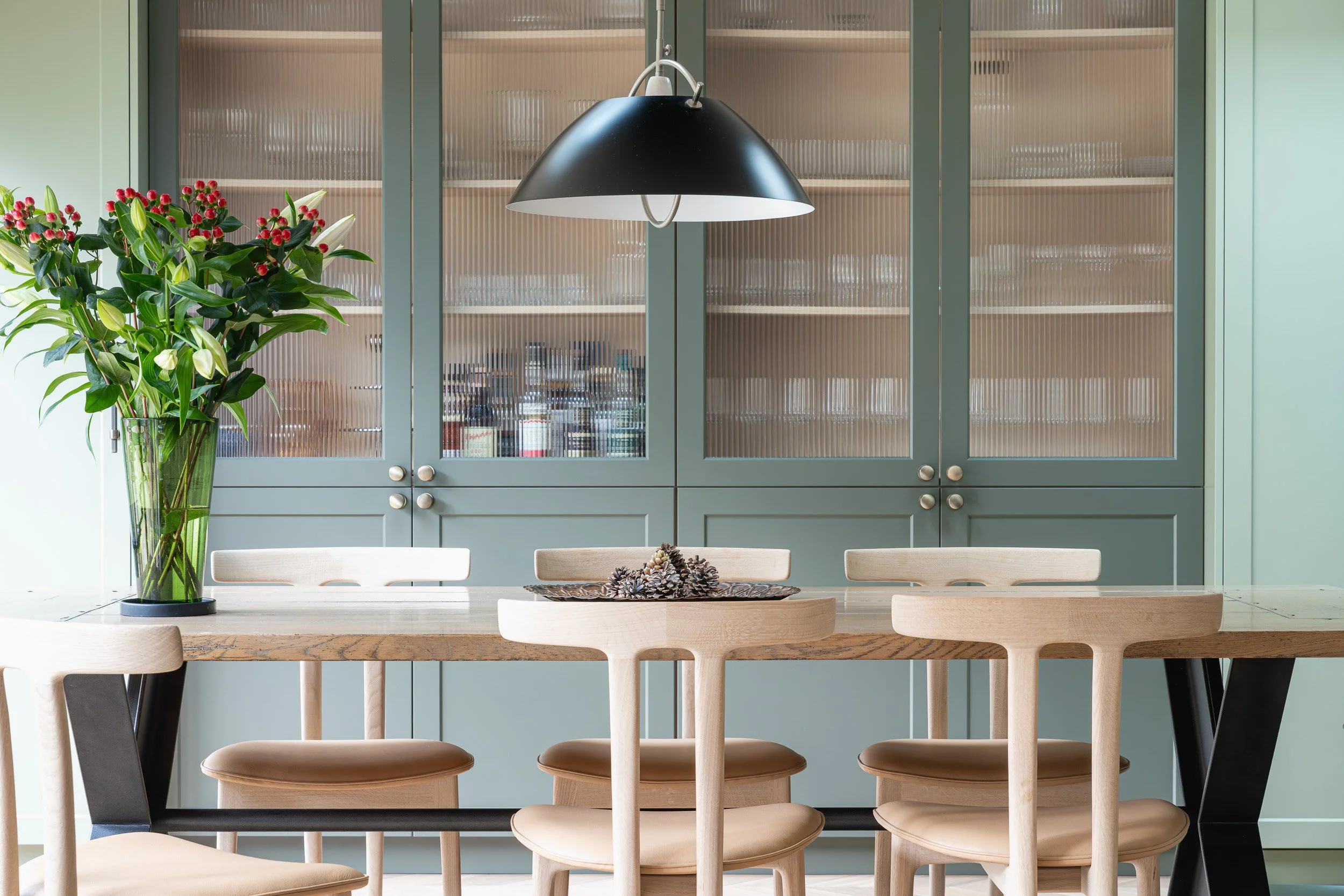 Green glazed kitchen cabinets behind a timber dining table