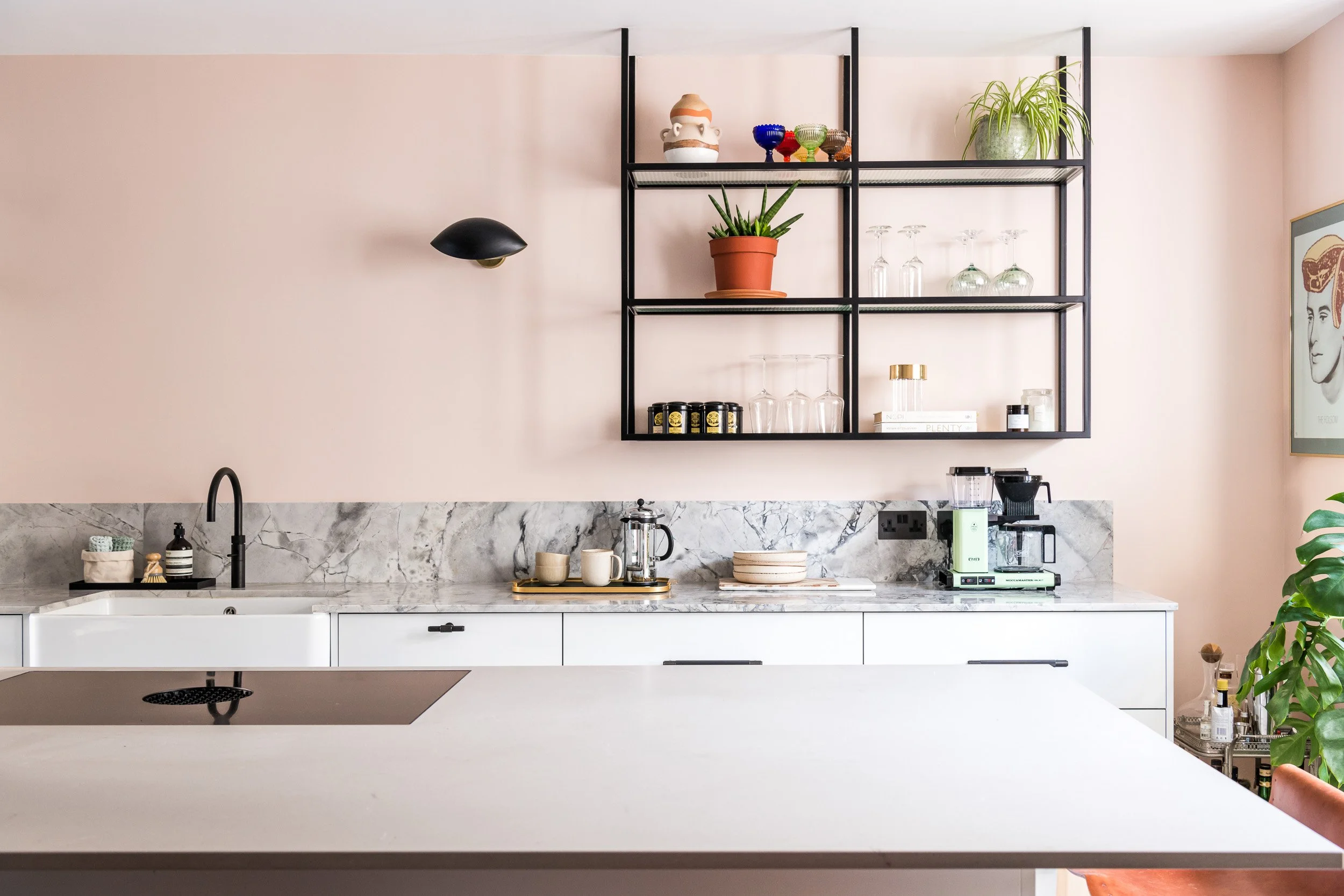 Kitchen with pale pink walls, a marble splashback and black metal shelving.