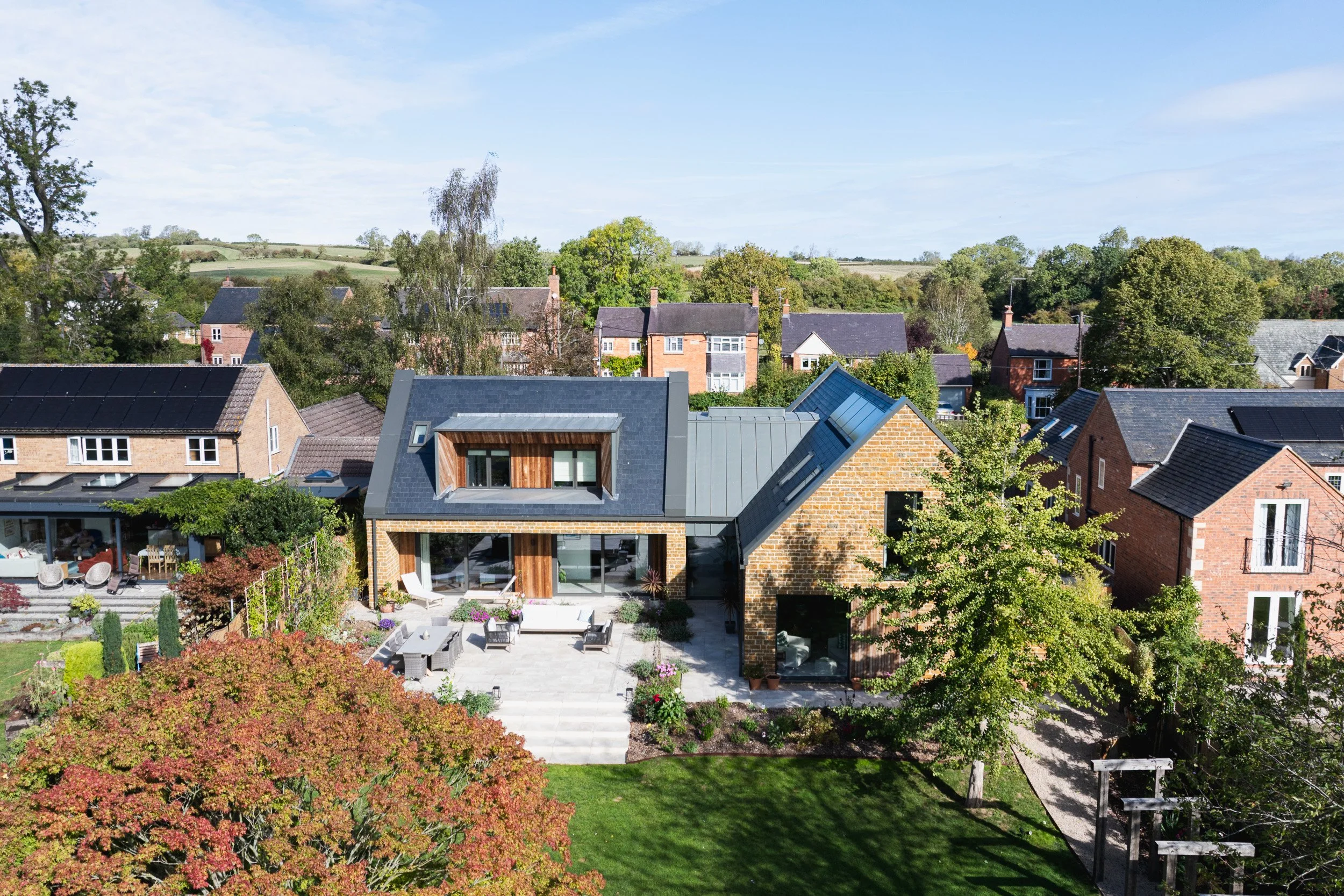 Elevated view of the house and terrace, with neighbouring homes, trees and countryside beyond.