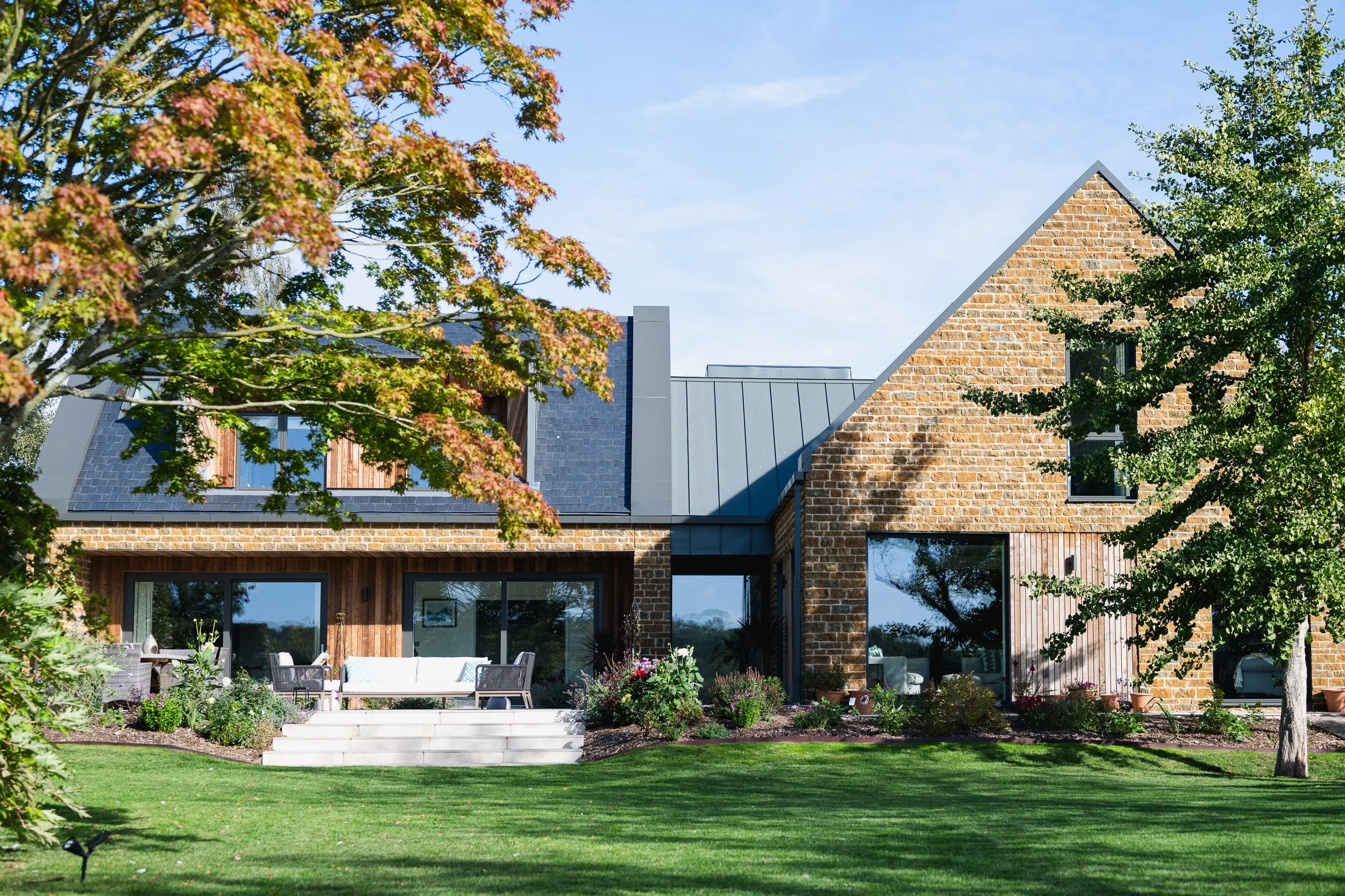 Stone and timber house with a terrace and lawn, framed by garden trees.