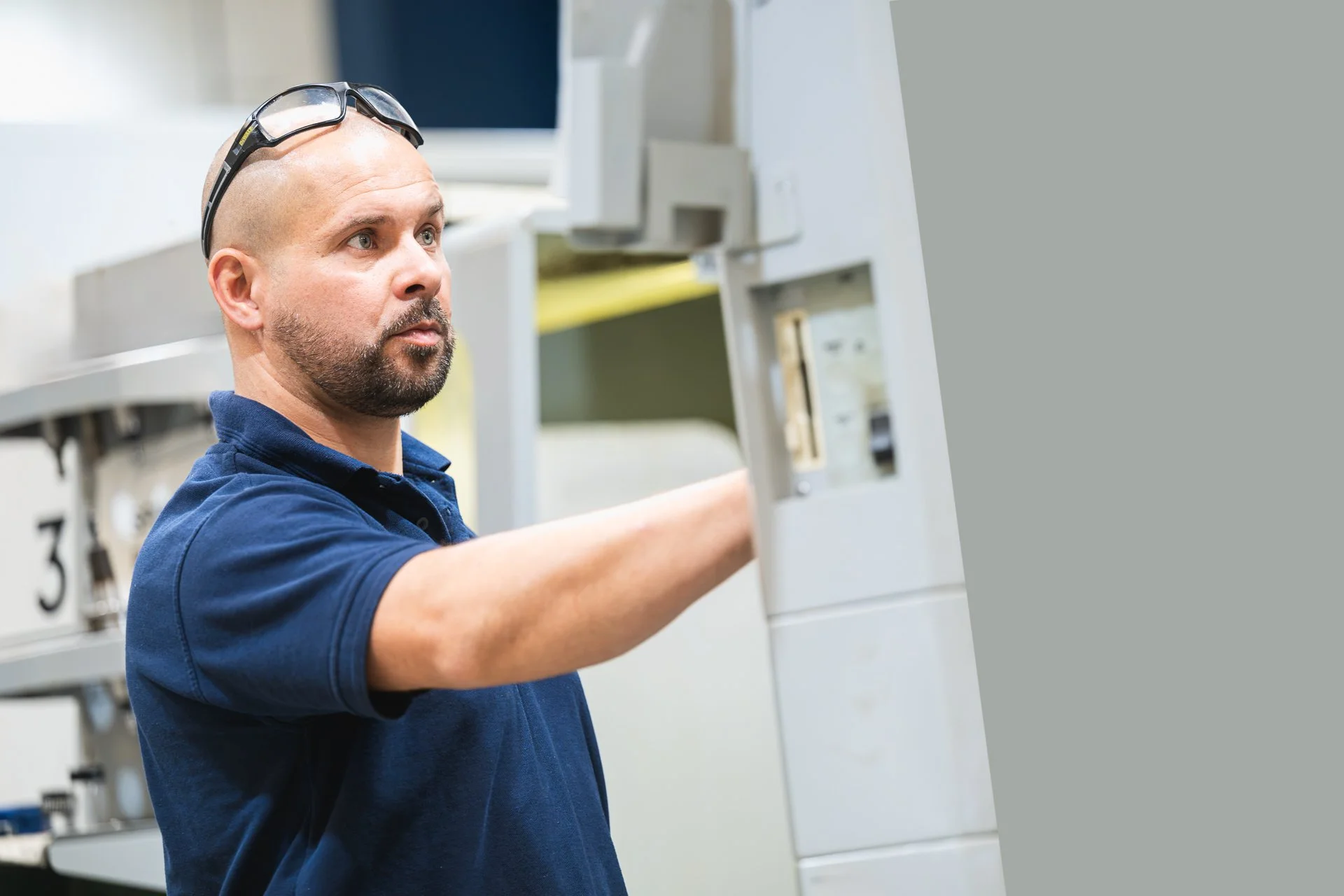 Team member in a navy polo shirt reaching towards a machine.