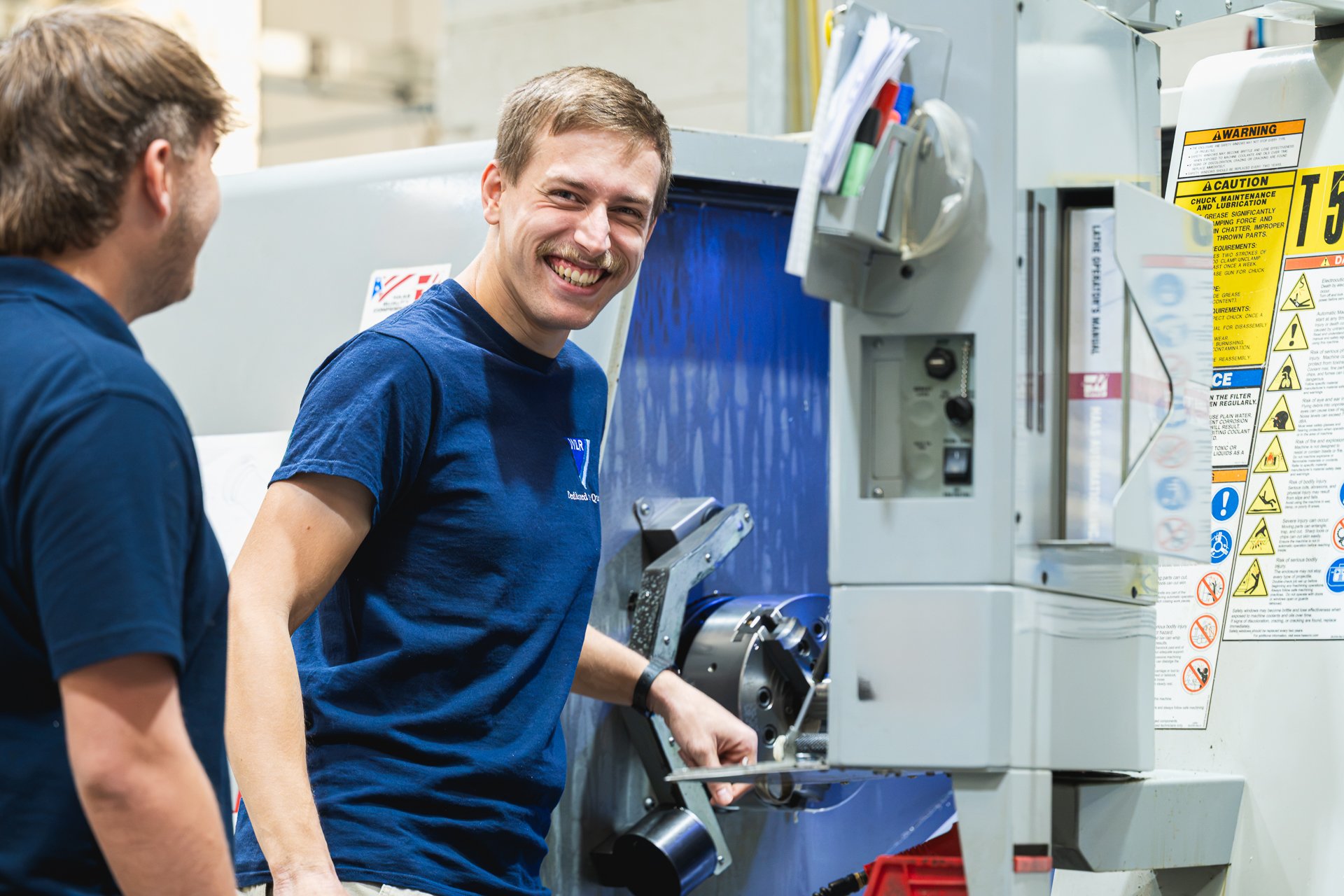 Two colleagues sharing a smile beside machinery at WLR Precision Engineering.