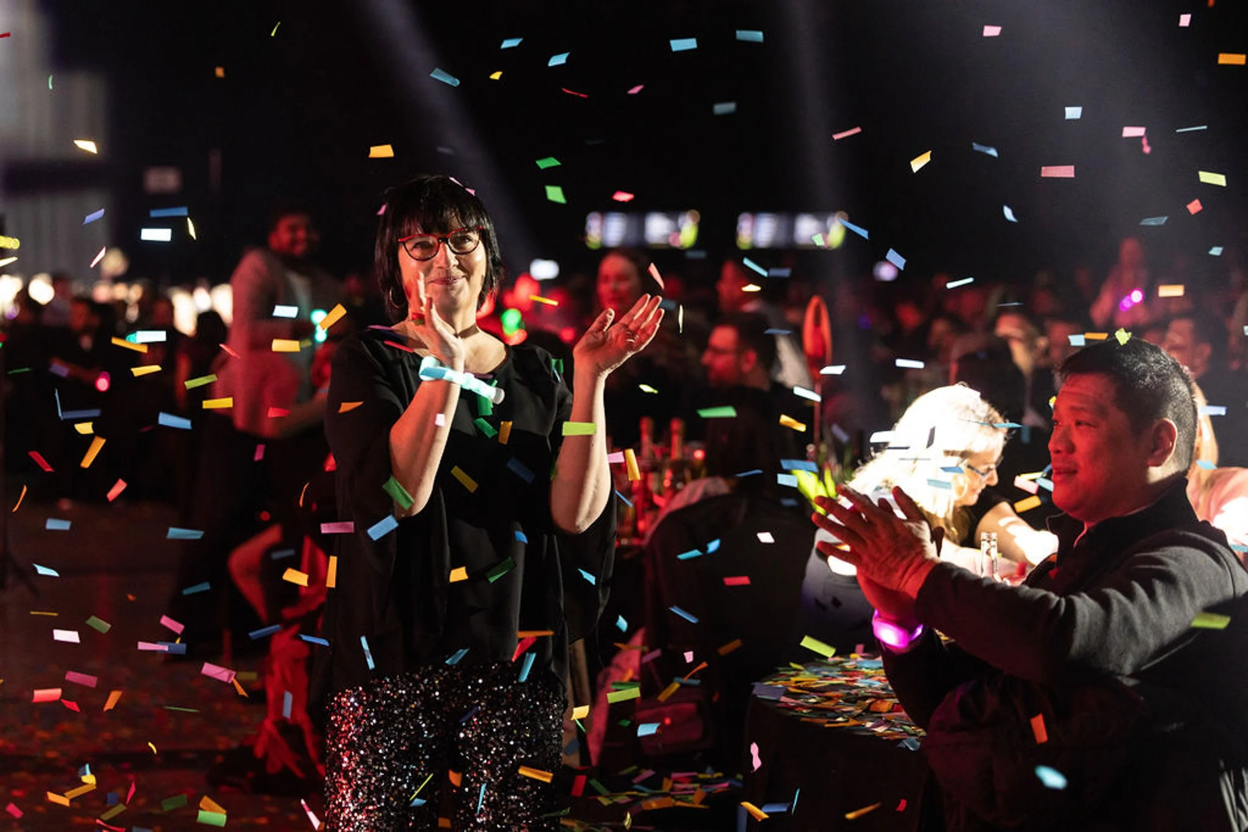 Guests applauding as multicoloured confetti falls around the dinner tables.