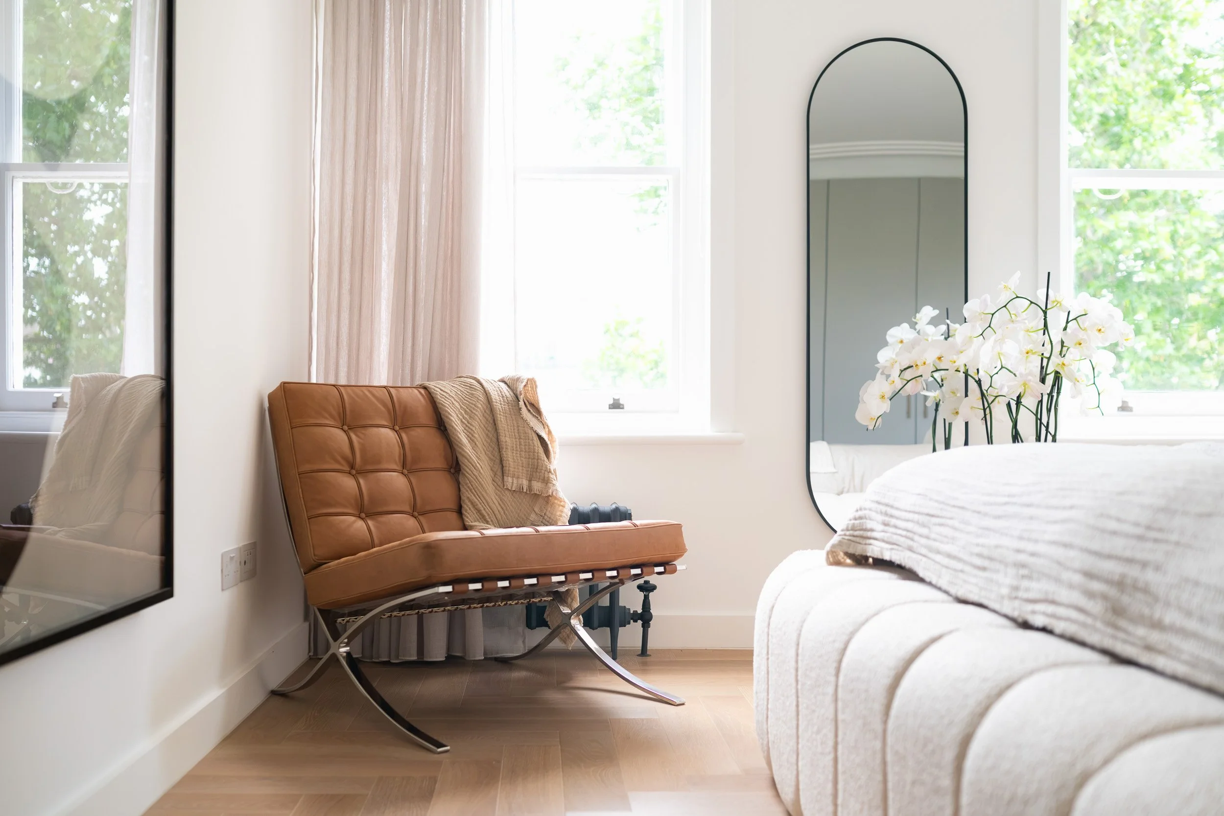 Tan chair and floor mirror beside a bedroom window