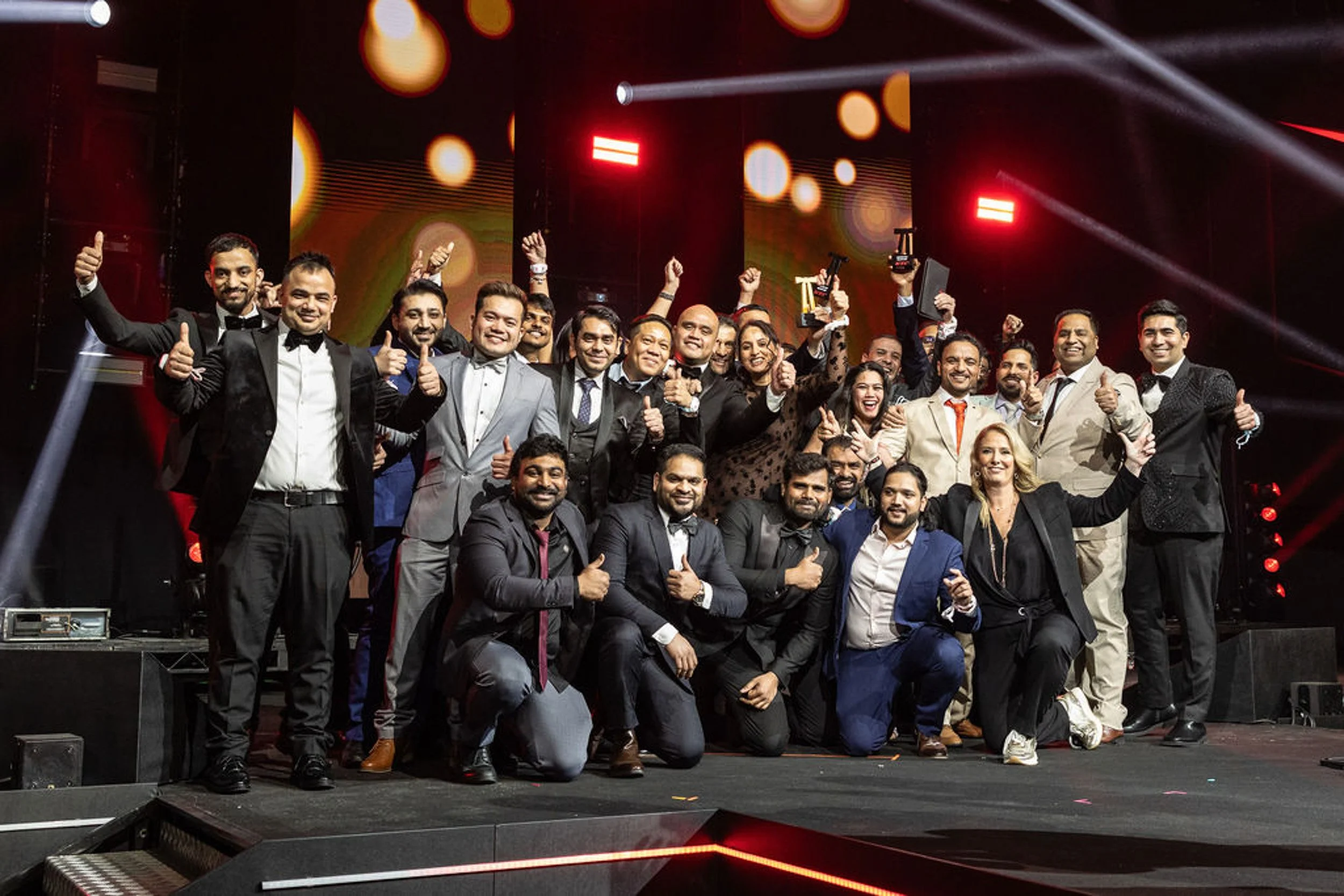 A large group posing on the KFC awards stage, with trophies held overhead.