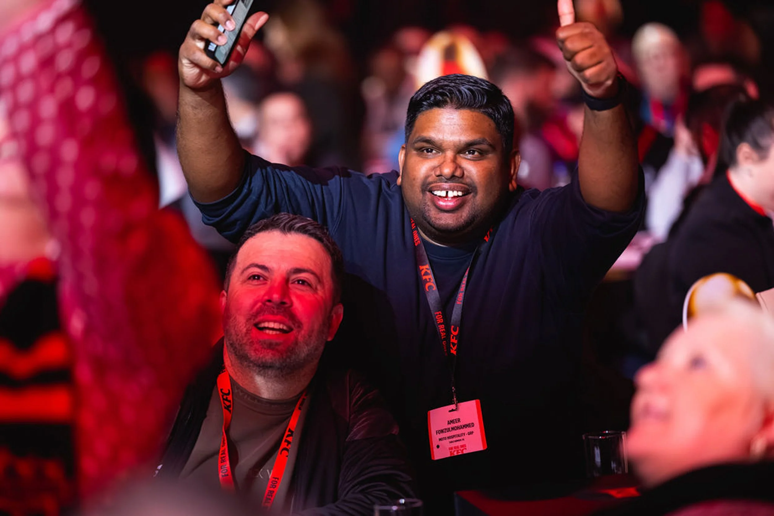 A KFC delegate raising both arms, holding a phone and giving a thumbs-up.