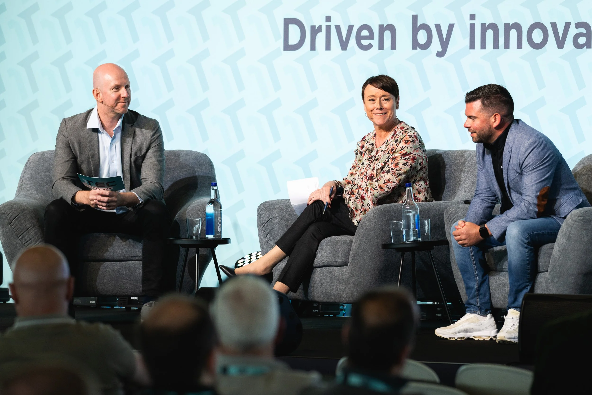 Three participants seated on stage during a 1TEC conference panel discussion.