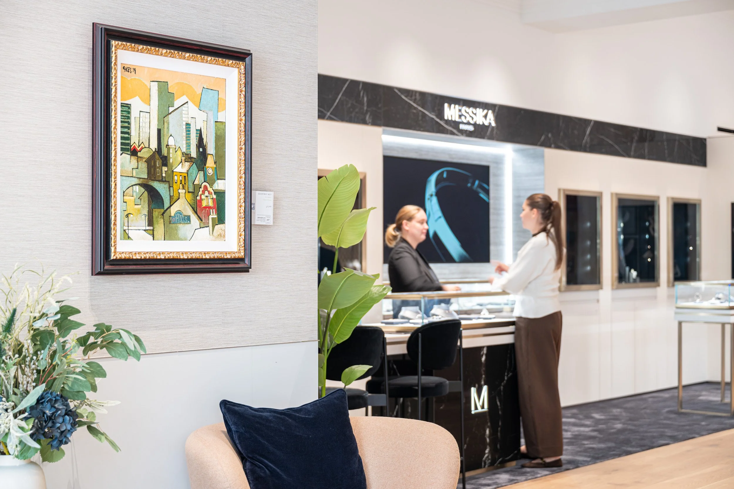 Framed painting beside the Messika display area, with two people at a counter.