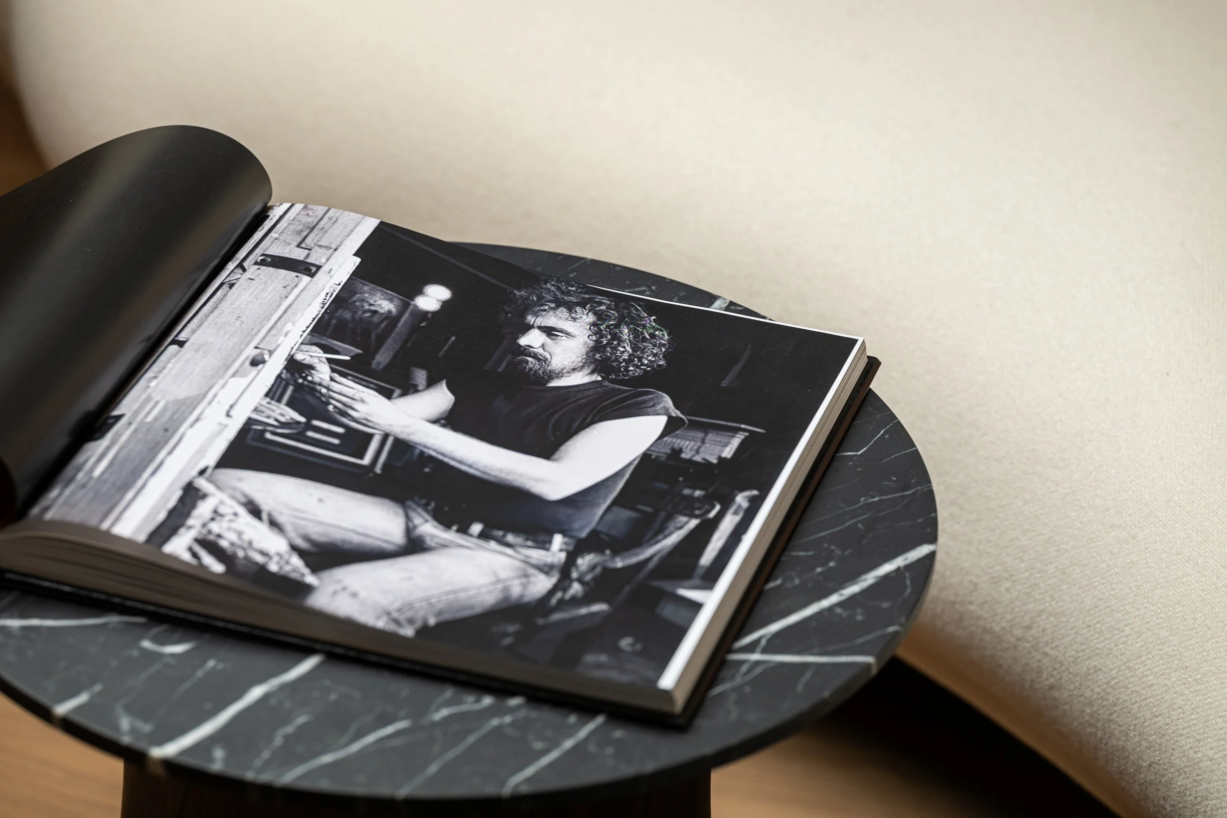 Open book showing a black-and-white photograph of an artist at work on a round dark table.
